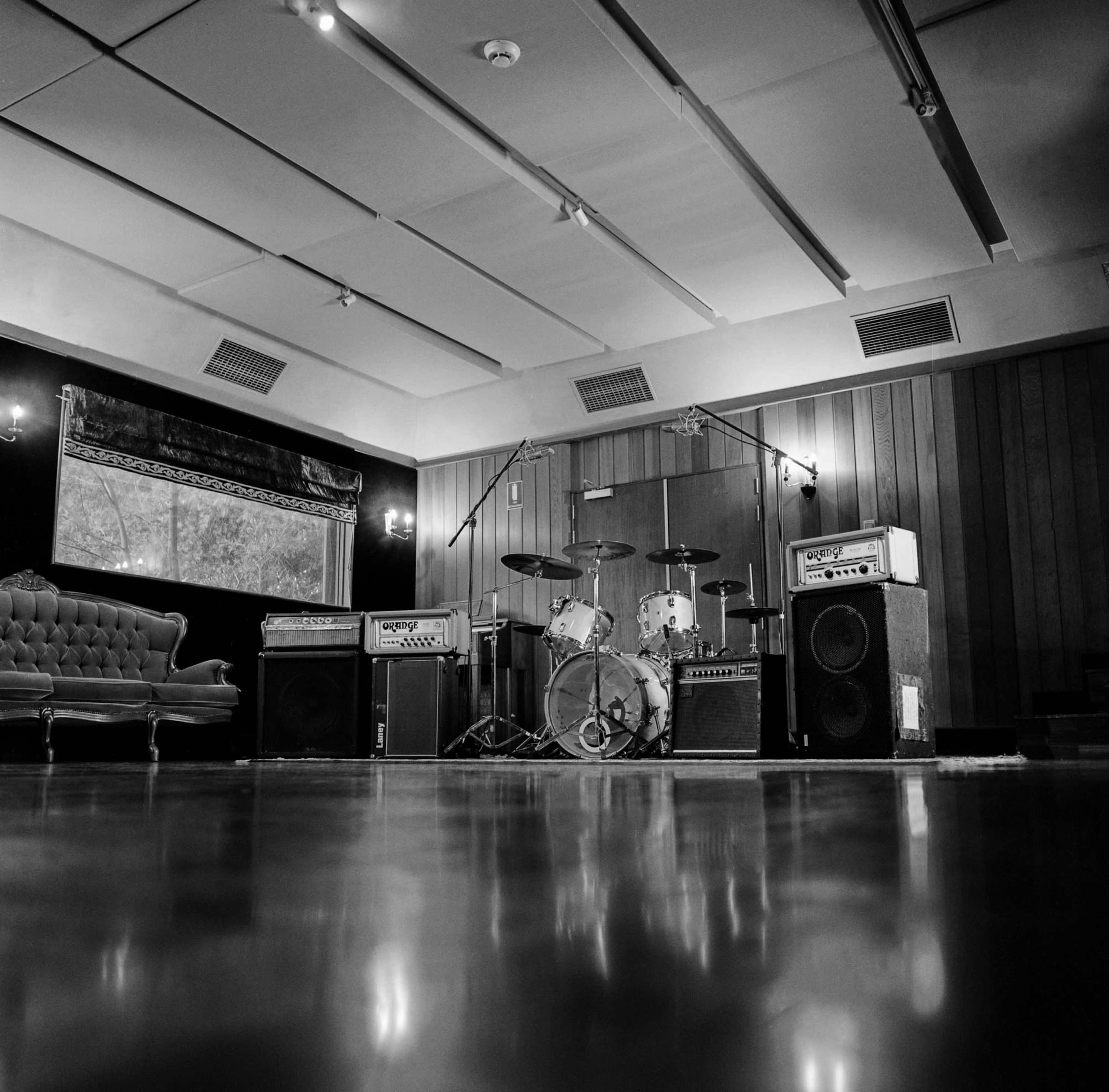 The image shows a music studio with a drum set, amplifiers, and a vintage couch in a spacious, polished room.