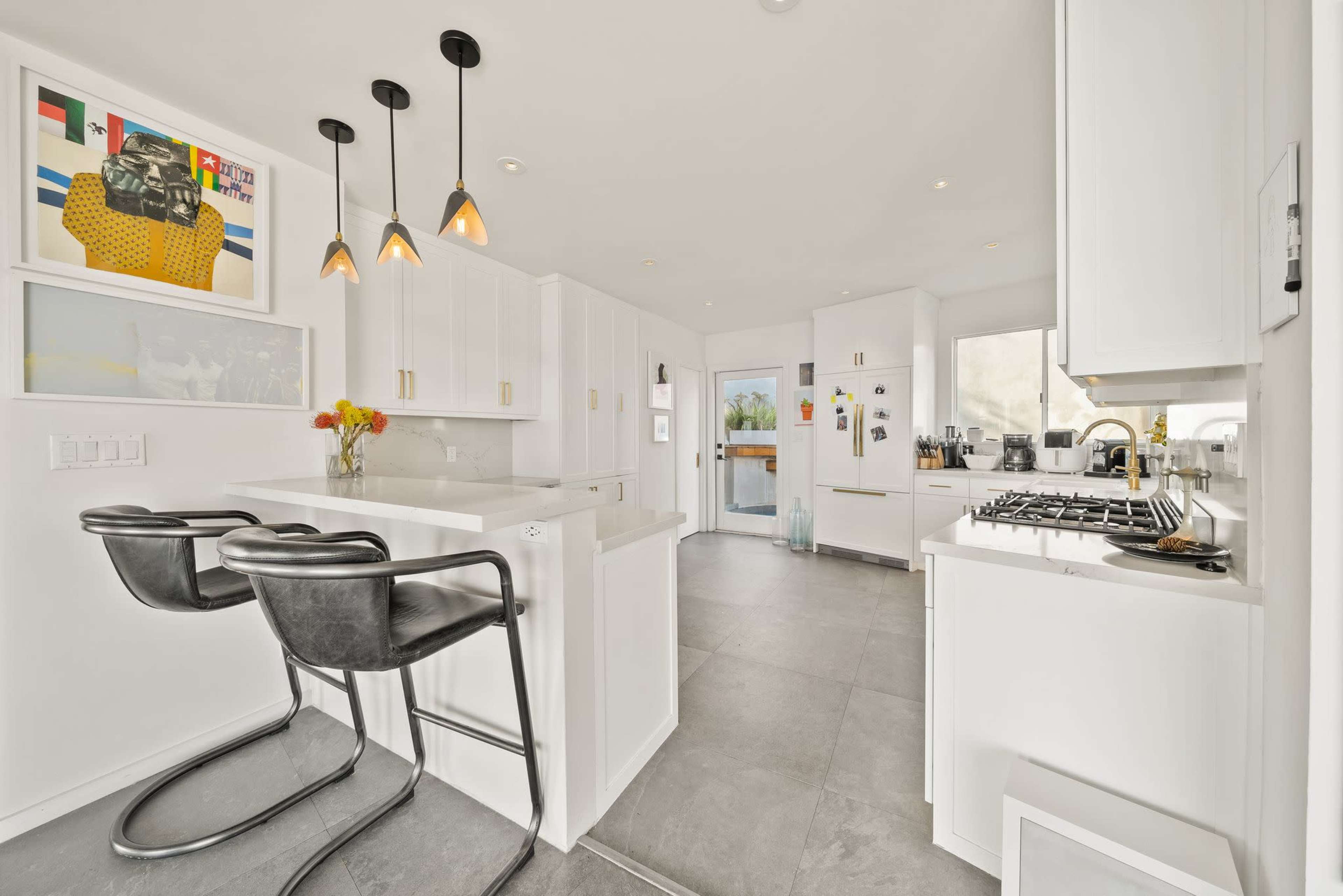 A modern kitchen features white cabinetry, a central island with two black stools, and pendant lighting.