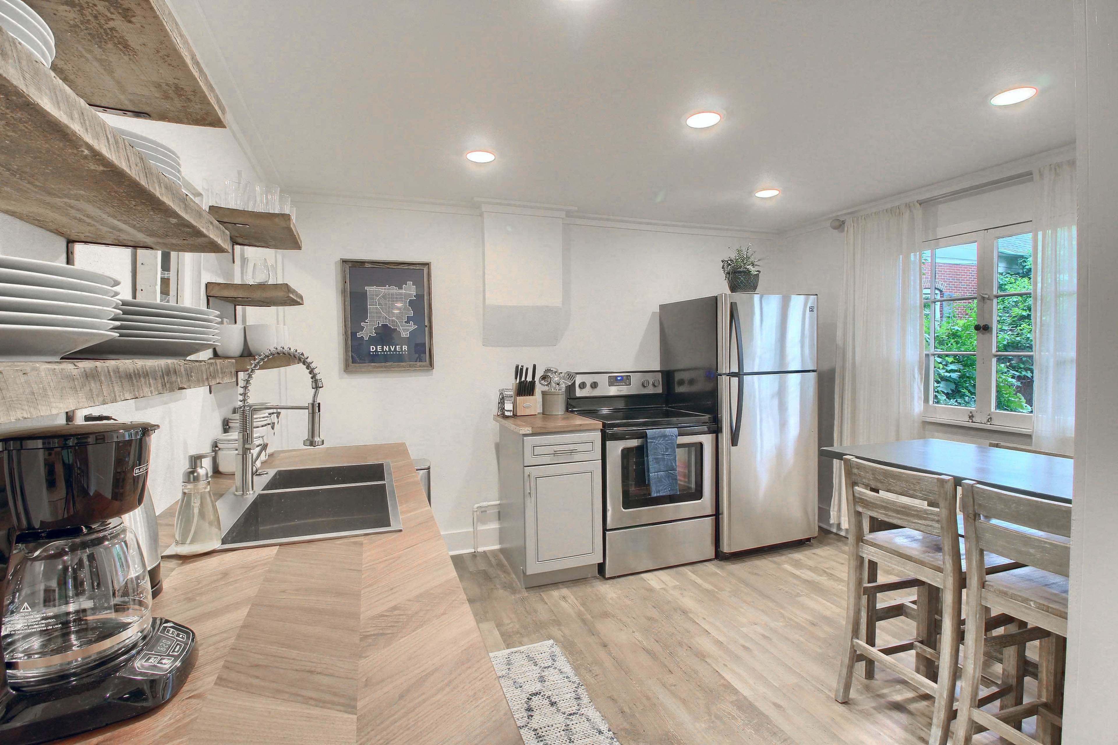 A modern kitchen with stainless steel appliances, open shelving with dishware, and a small dining table with wooden chairs.