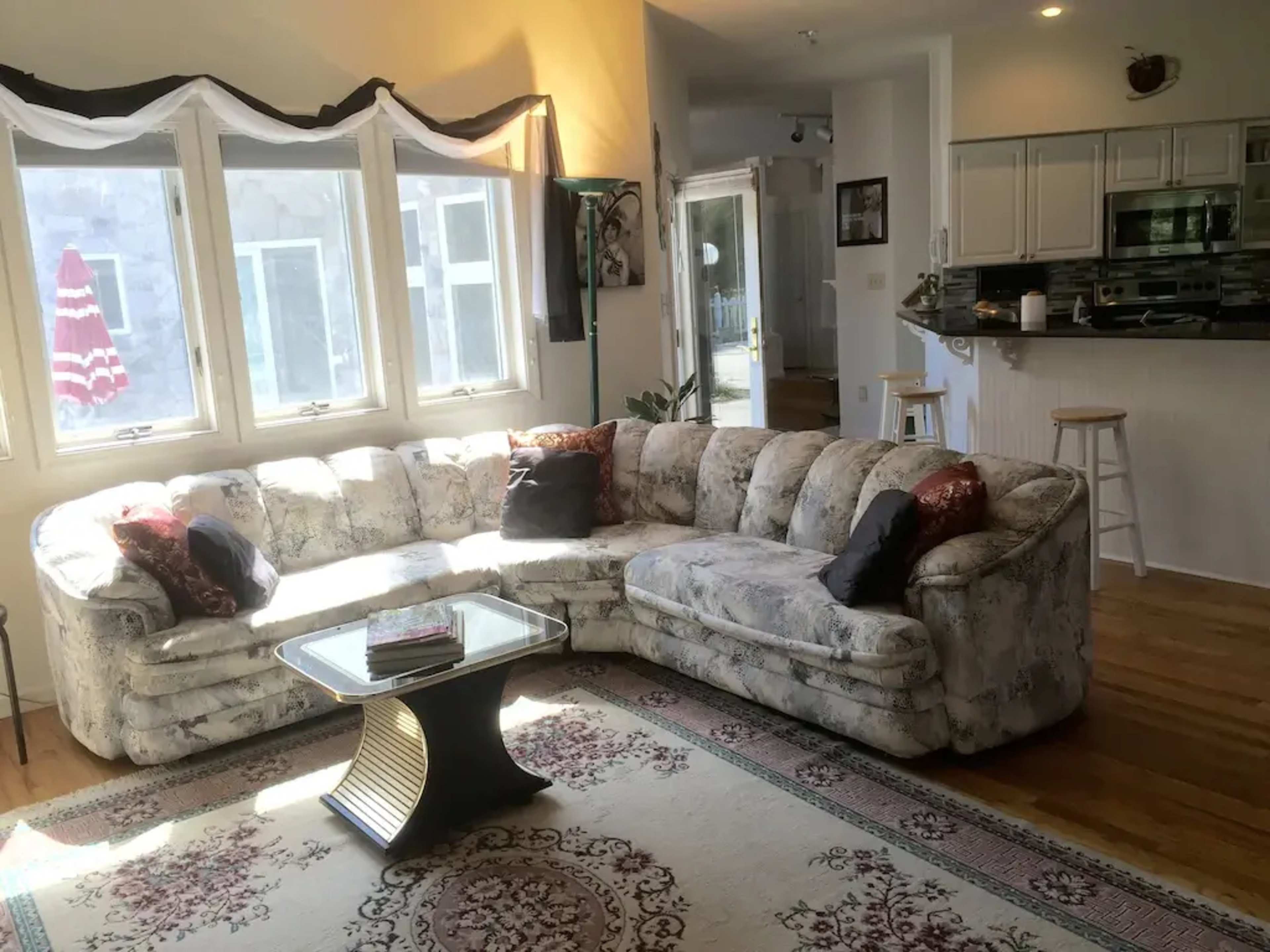 A living room with a large sectional sofa, a glass coffee table, and a view of an outdoor area through the windows.