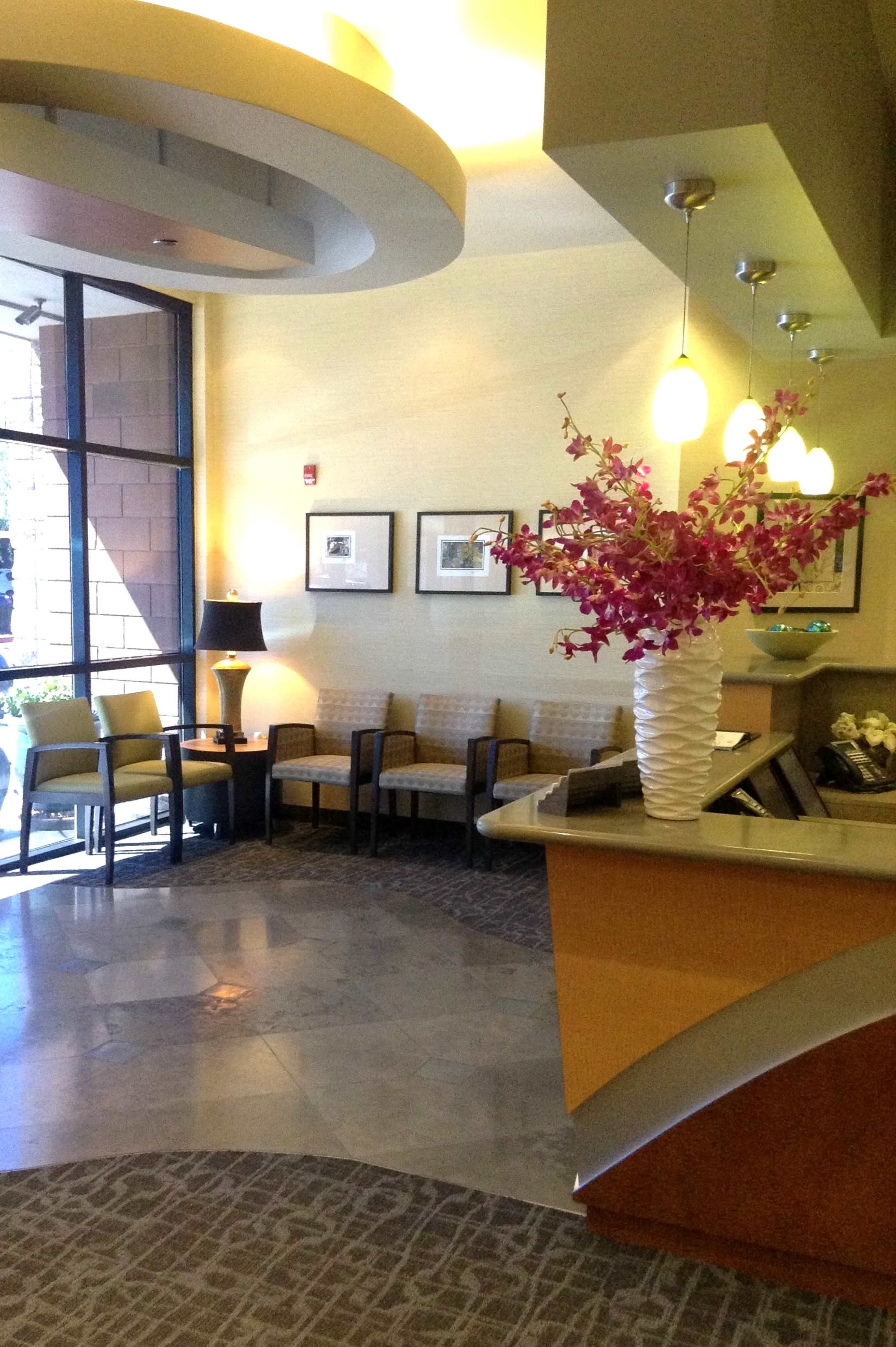 The image depicts a modern reception area with a vase of pink flowers, seating arrangements, and a front desk.