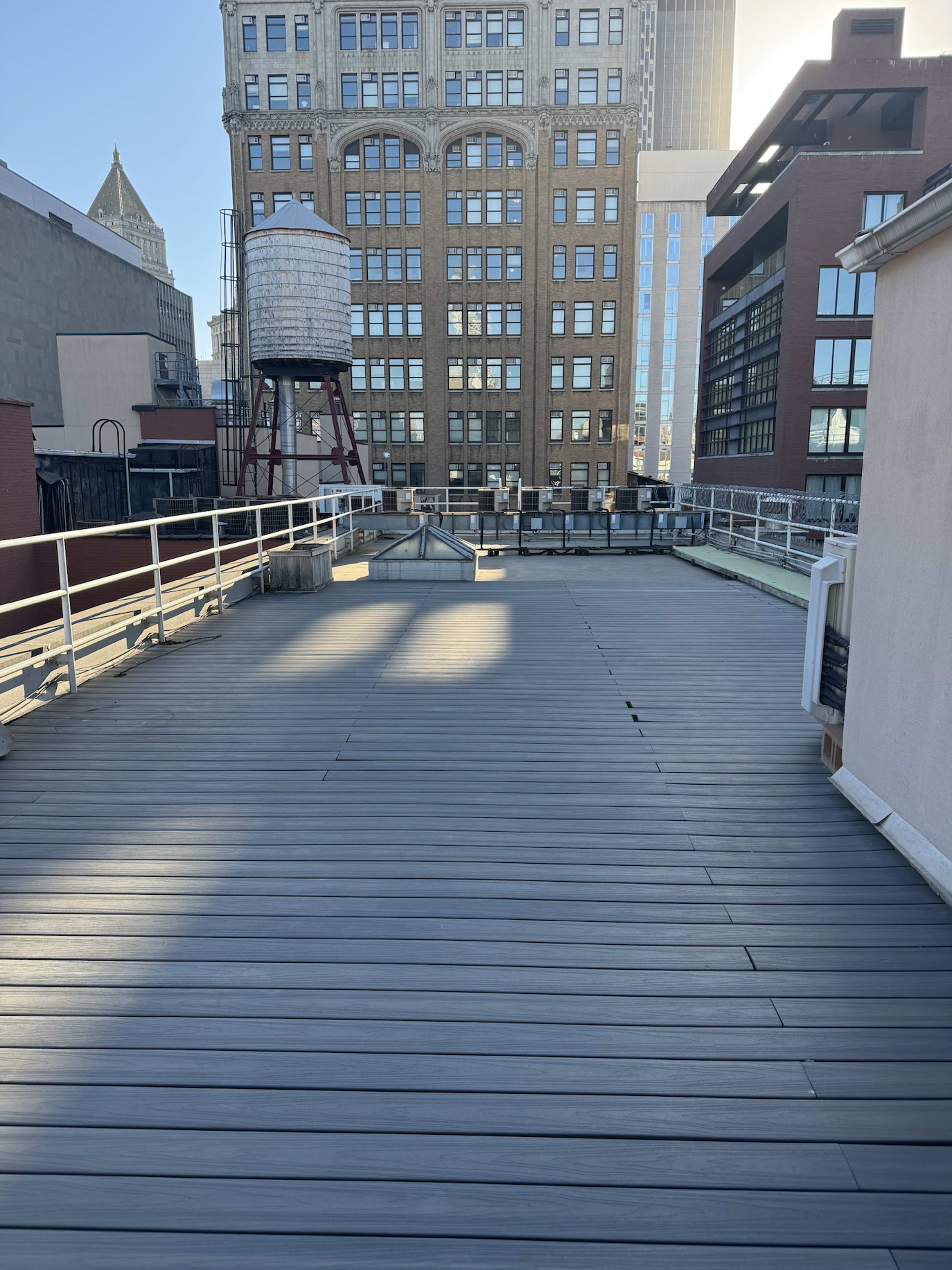 A flat rooftop surface made of wooden planks stretches out toward a skyline featuring buildings and a water tower in the background.