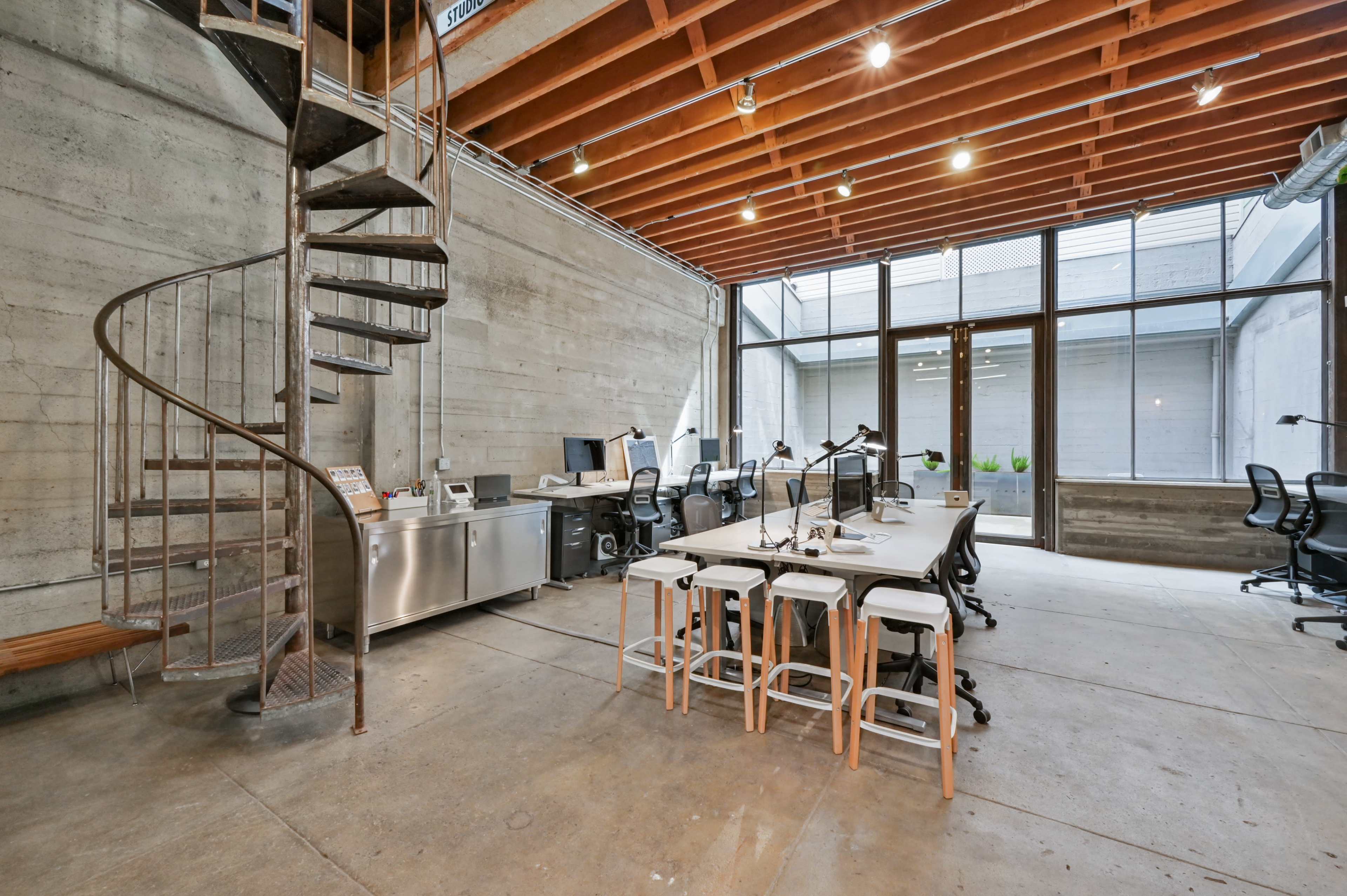A modern office space with a spiral staircase, a large table surrounded by chairs, and several workstations equipped with computers.