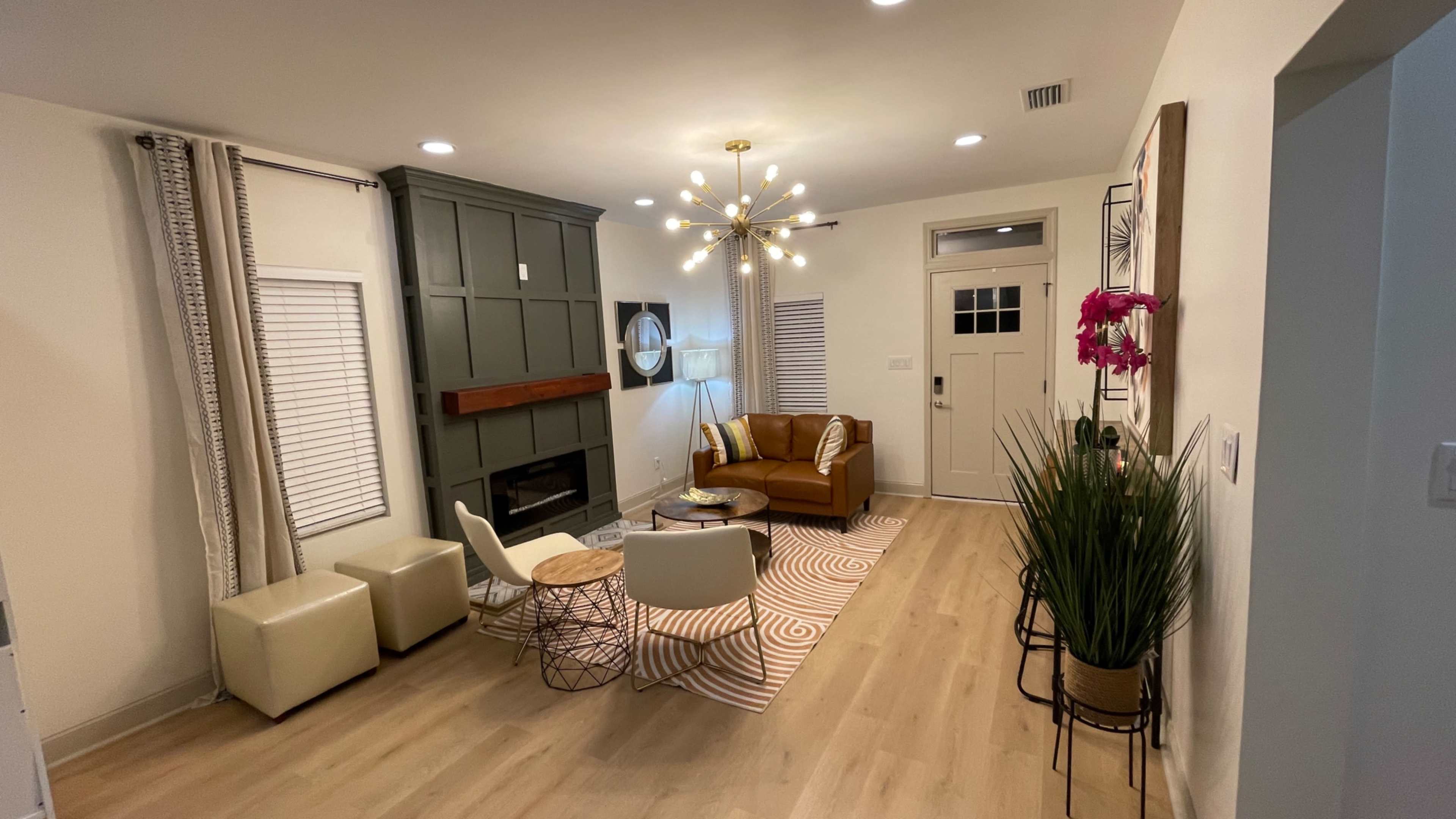 A modern living room featuring a brown leather sofa, a round coffee table, and a geometric rug, with a wall-mounted fireplace and a striking light fixture.