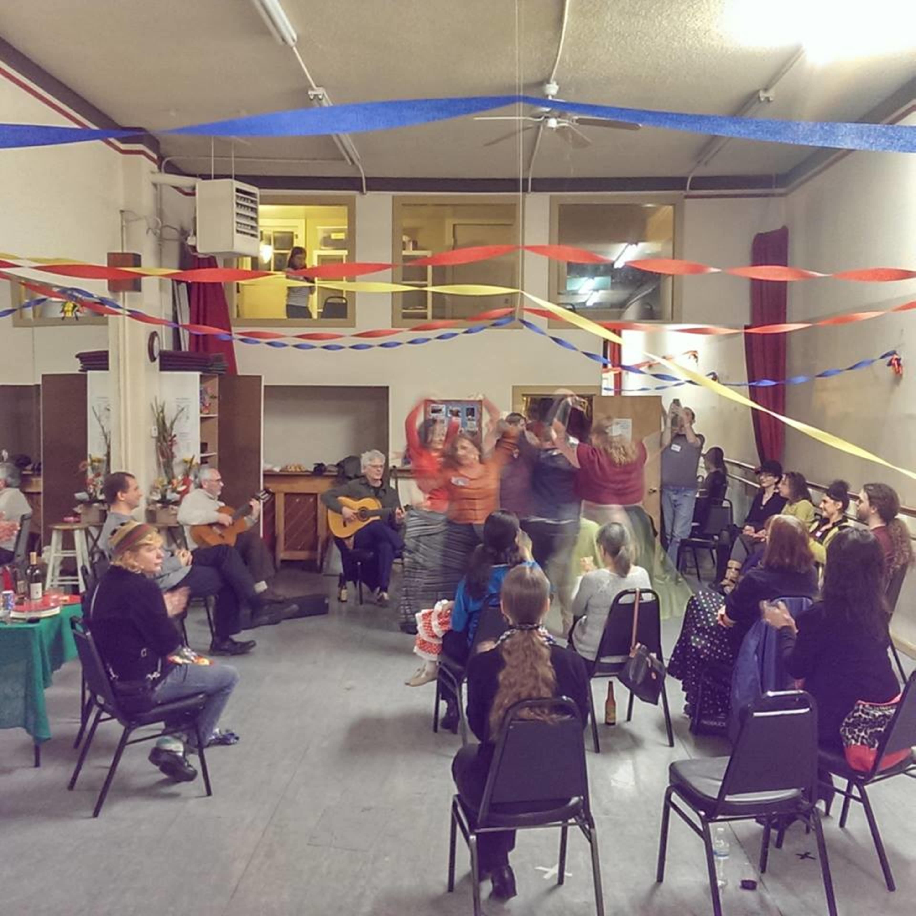 A group of people dance in a decorated room filled with colorful streamers while others sit and watch.