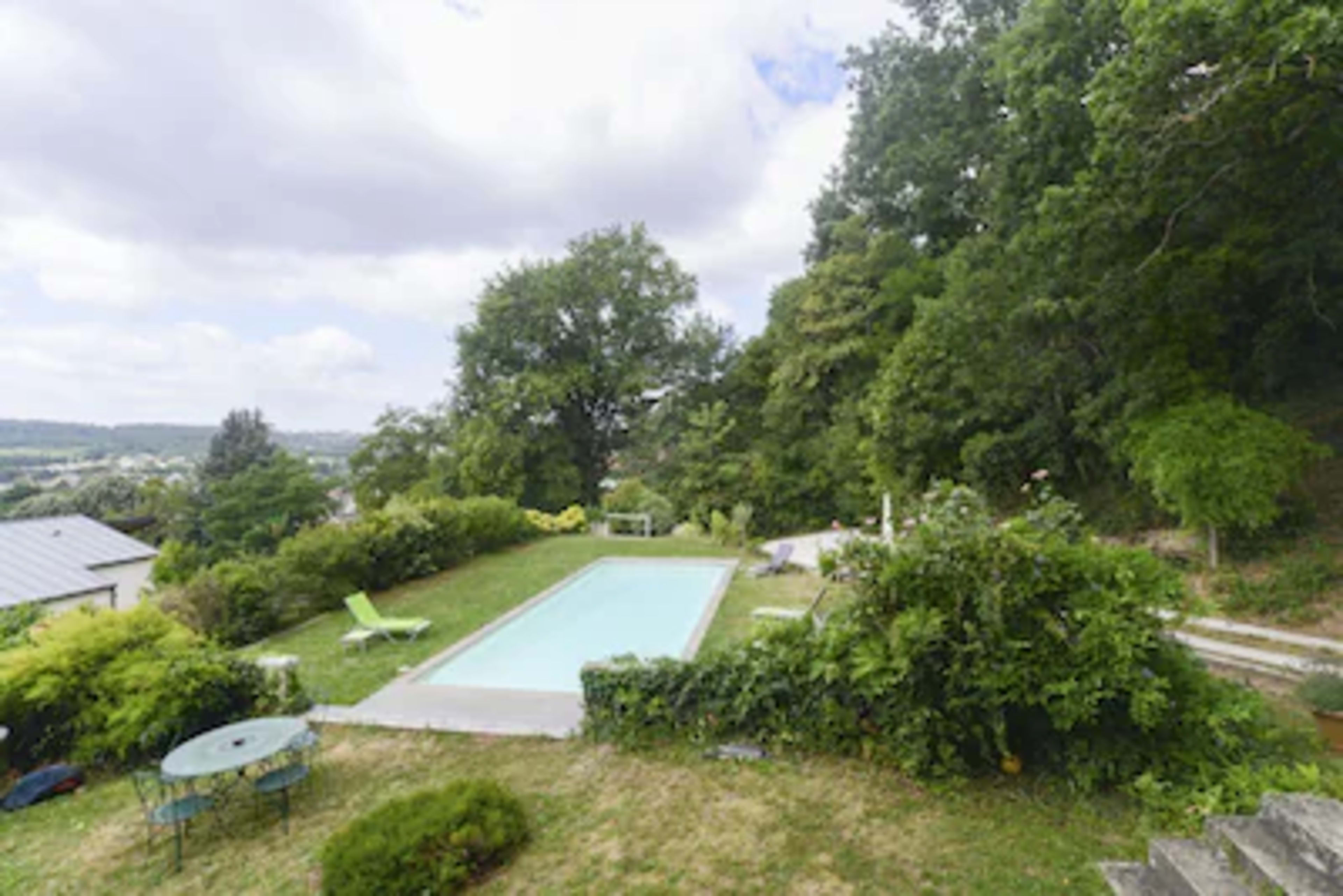 A swimming pool is surrounded by greenery and outdoor seating in a landscaped garden.