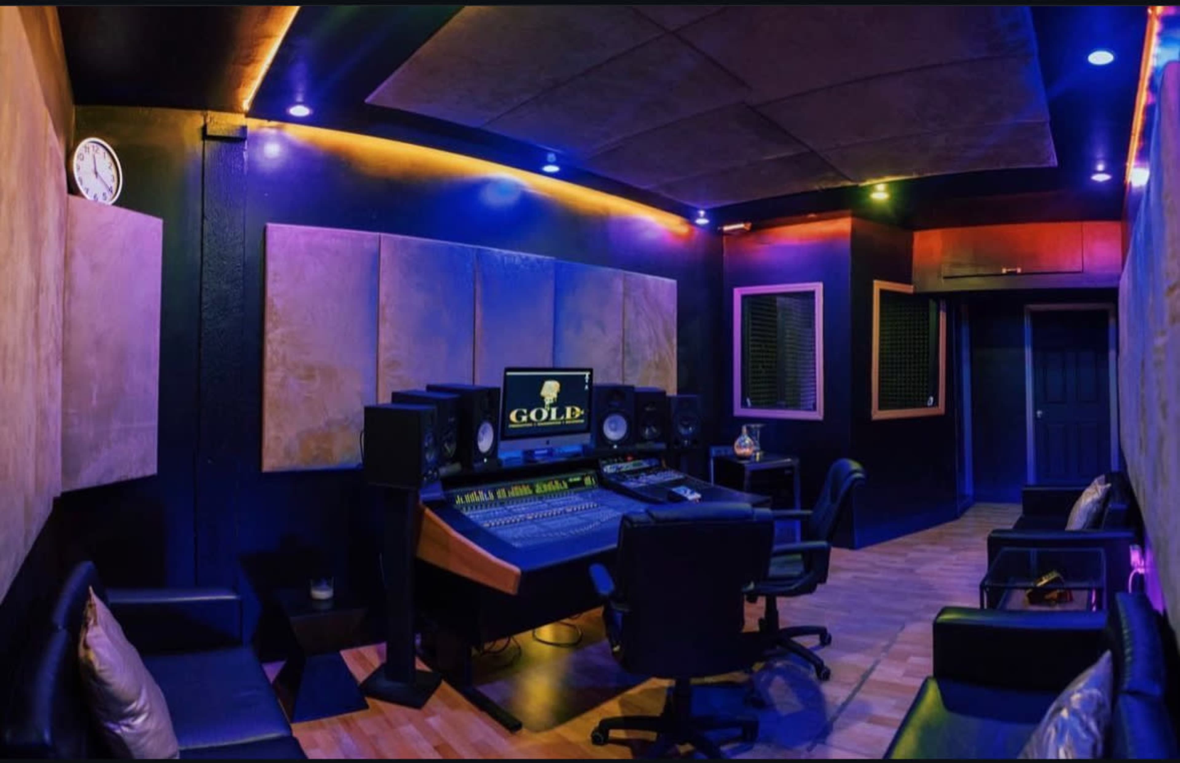 A modern music recording studio with a central mixing desk, speakers, and soundproof panels on the walls.