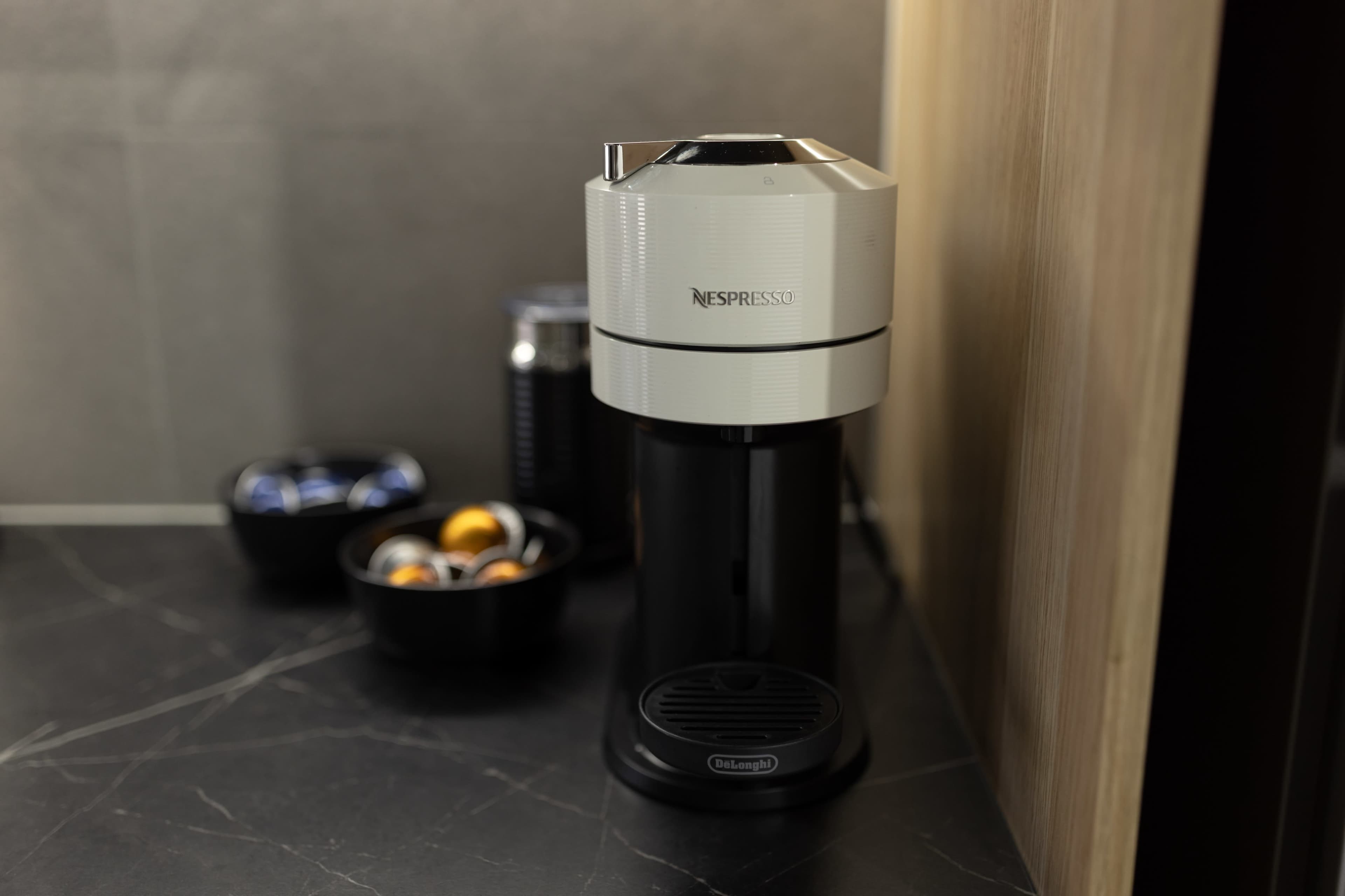 A Nespresso coffee machine sits on a dark countertop next to bowls containing coffee capsules.