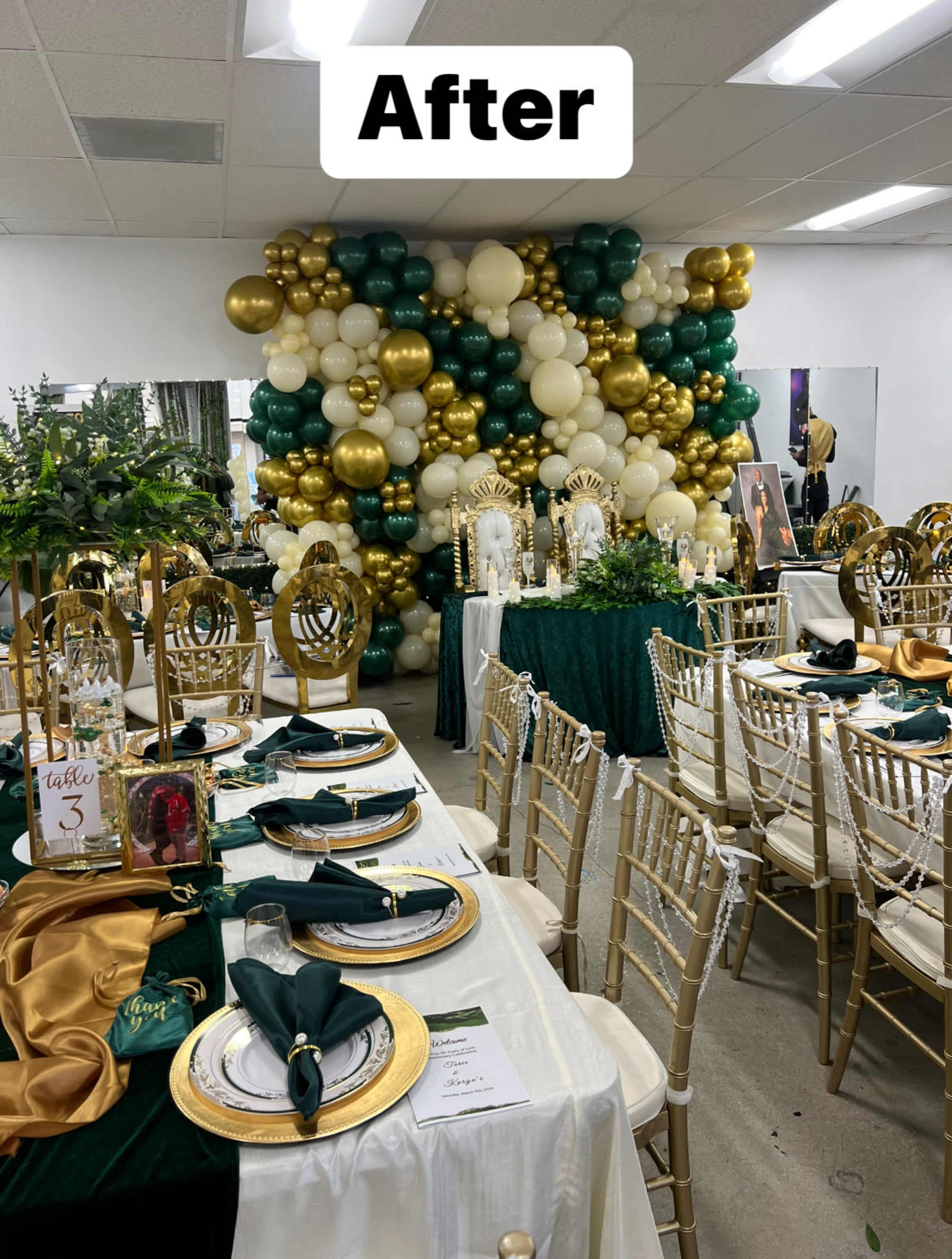 A decorated banquet room with a table setup featuring gold and green tableware, surrounded by a wall of balloons and floral arrangements.