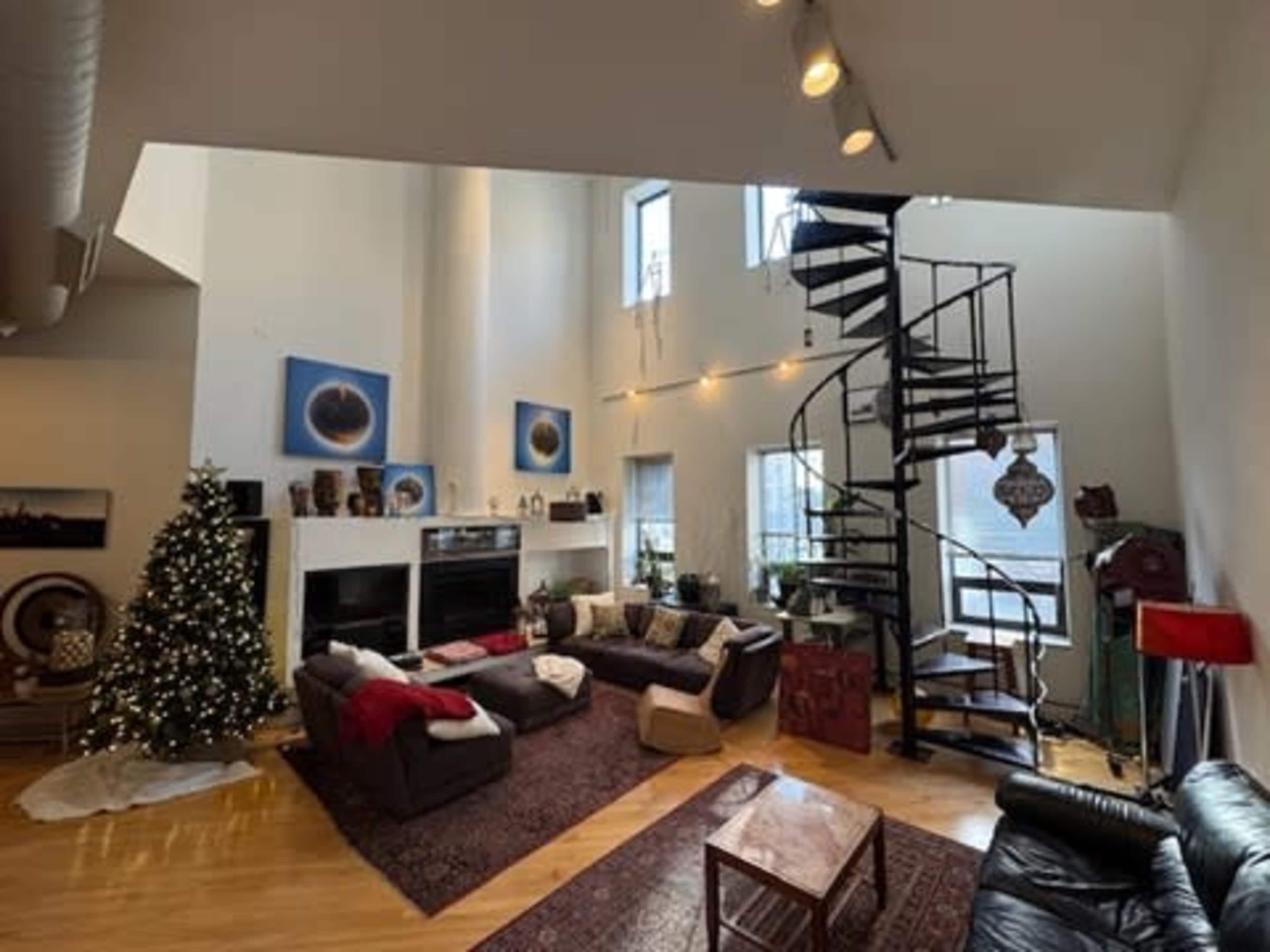 The spacious living room features a spiral staircase, a large window, a Christmas tree, and various pieces of modern art on the walls.