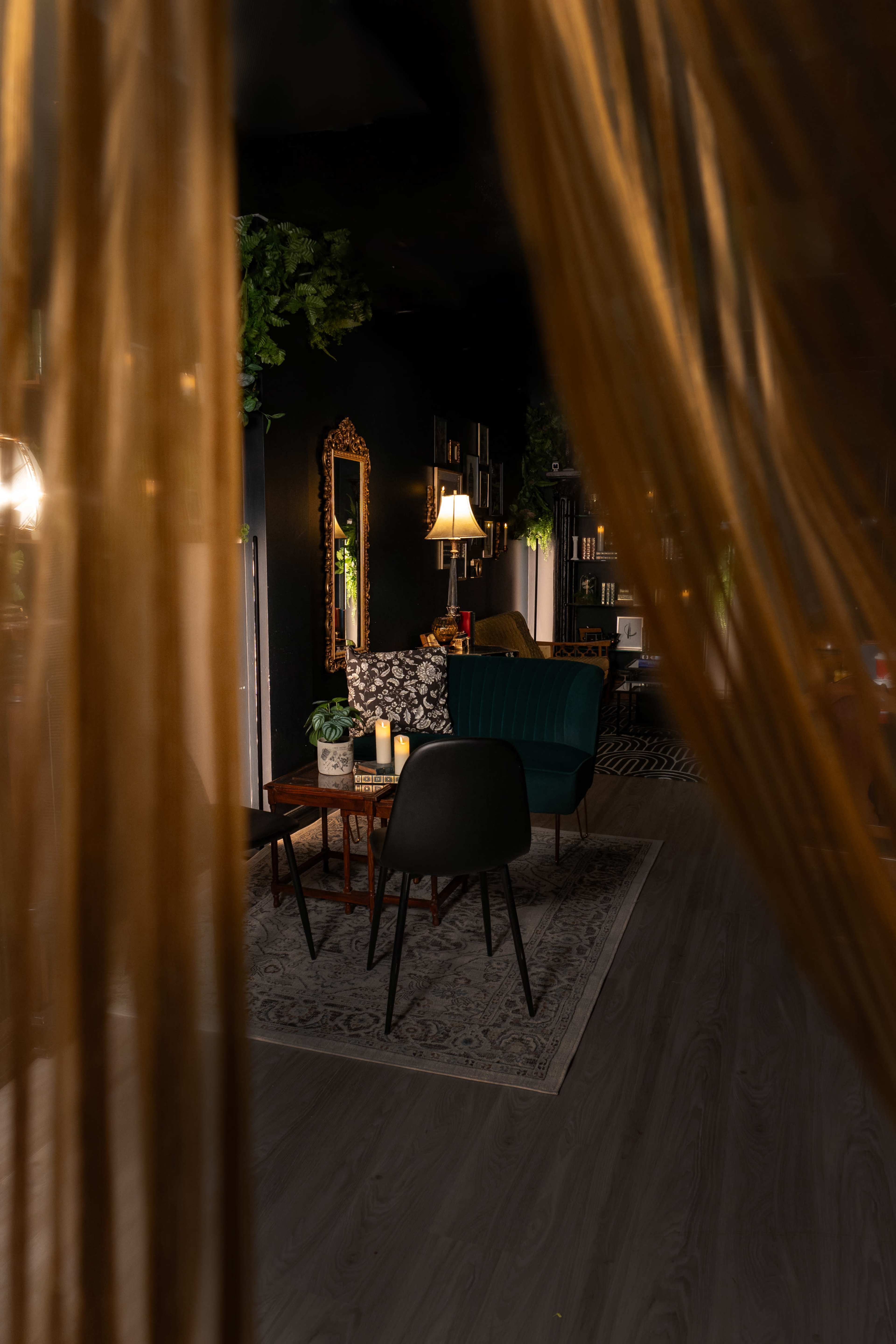 A cozy seating area with a green sofa, a coffee table, and a floor lamp, framed by sheer curtains.