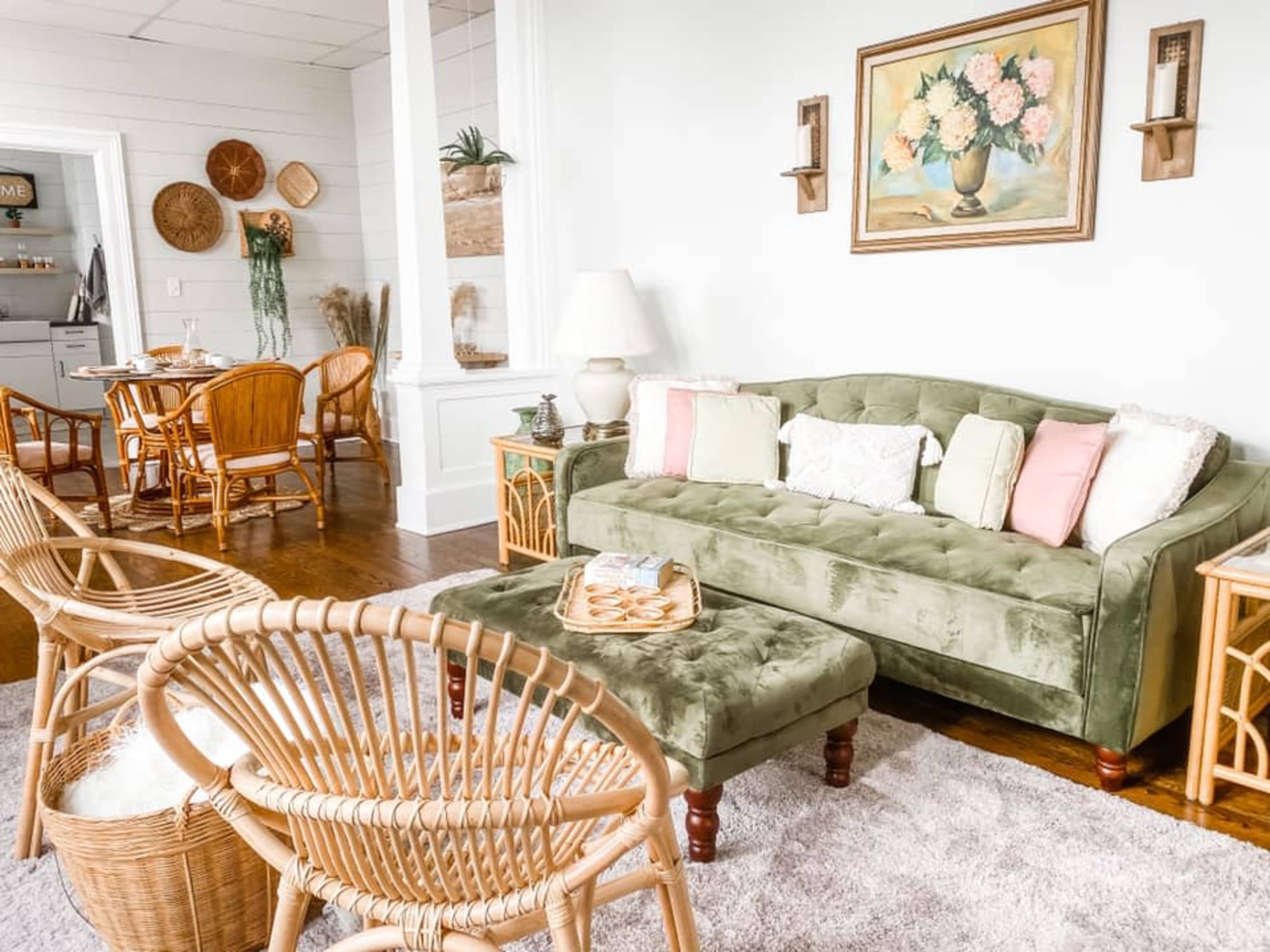 A cozy living room with a green sofa, wicker chairs, and a coffee table, arranged around a light-colored rug.