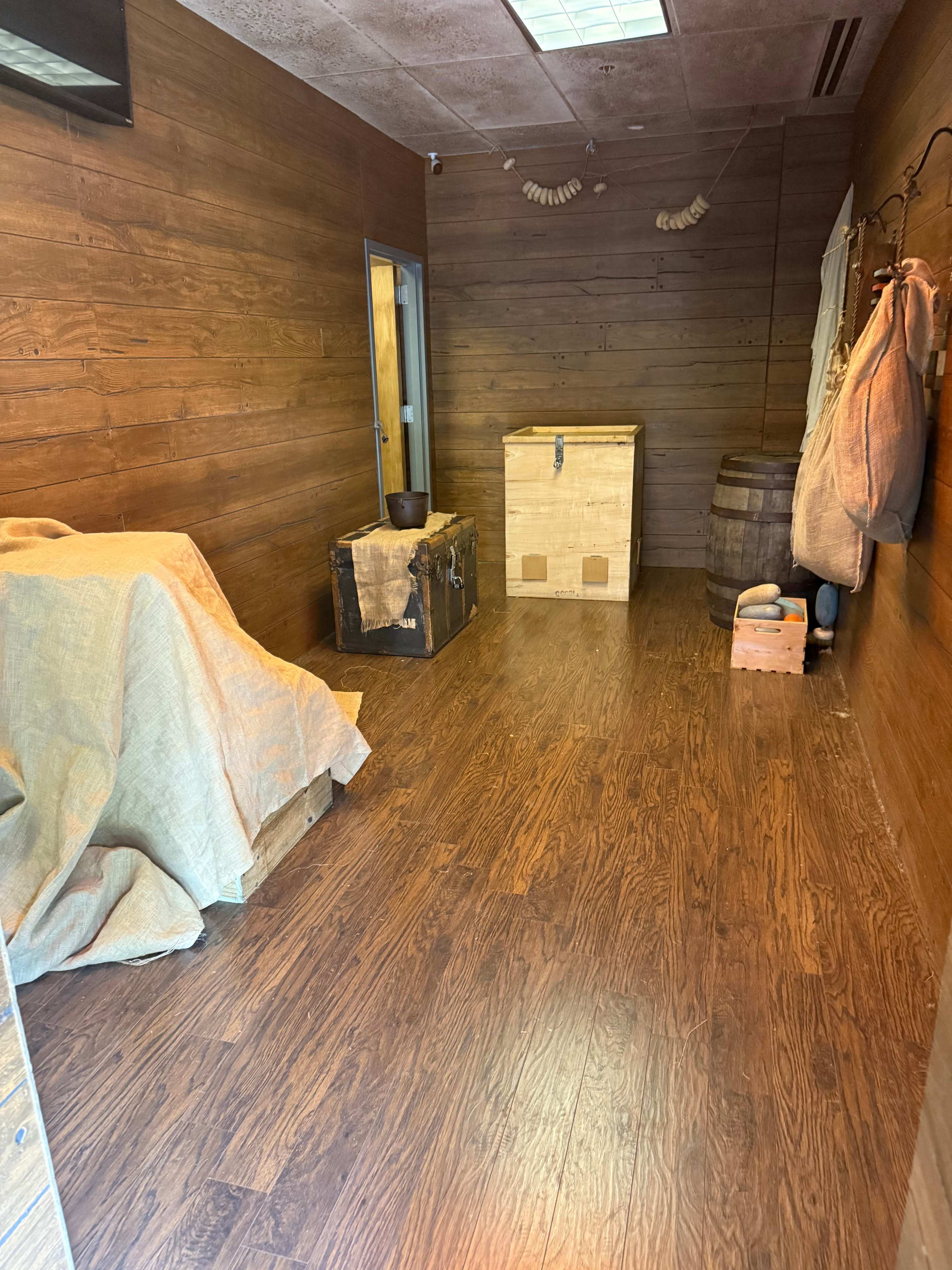 The interior features wooden walls and flooring, with a wooden box, a chest, and a barrel present in the empty space.