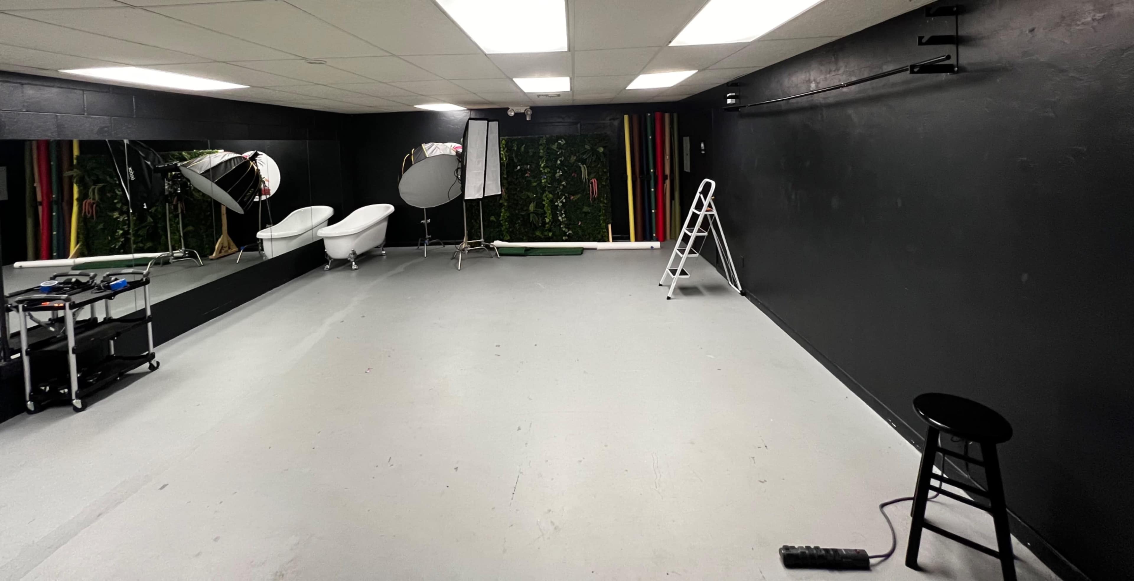 A spacious photography studio featuring a black wall, two large mirrors, a ladder, and equipment carts.