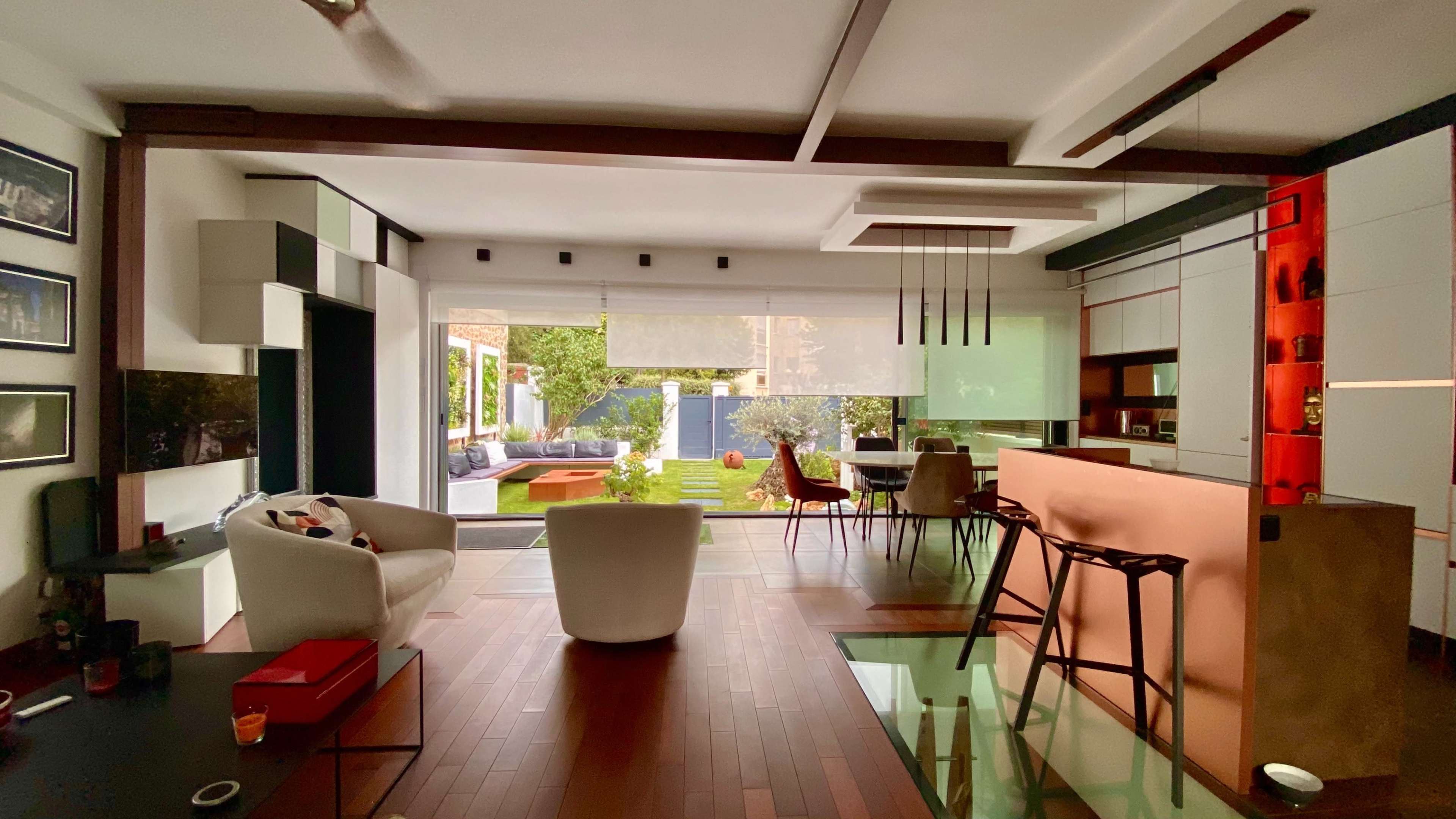 A modern living space with a kitchen and dining area that opens up to a landscaped backyard through large glass doors.