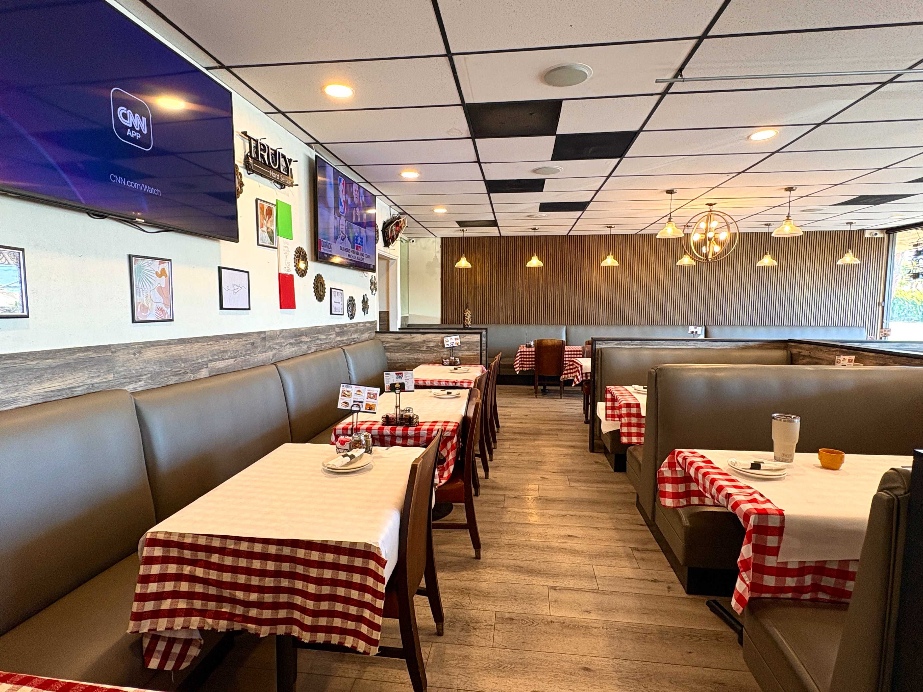 The image shows the interior of a restaurant featuring booths with checkered tablecloths, a television on the wall, and a wooden accent wall.