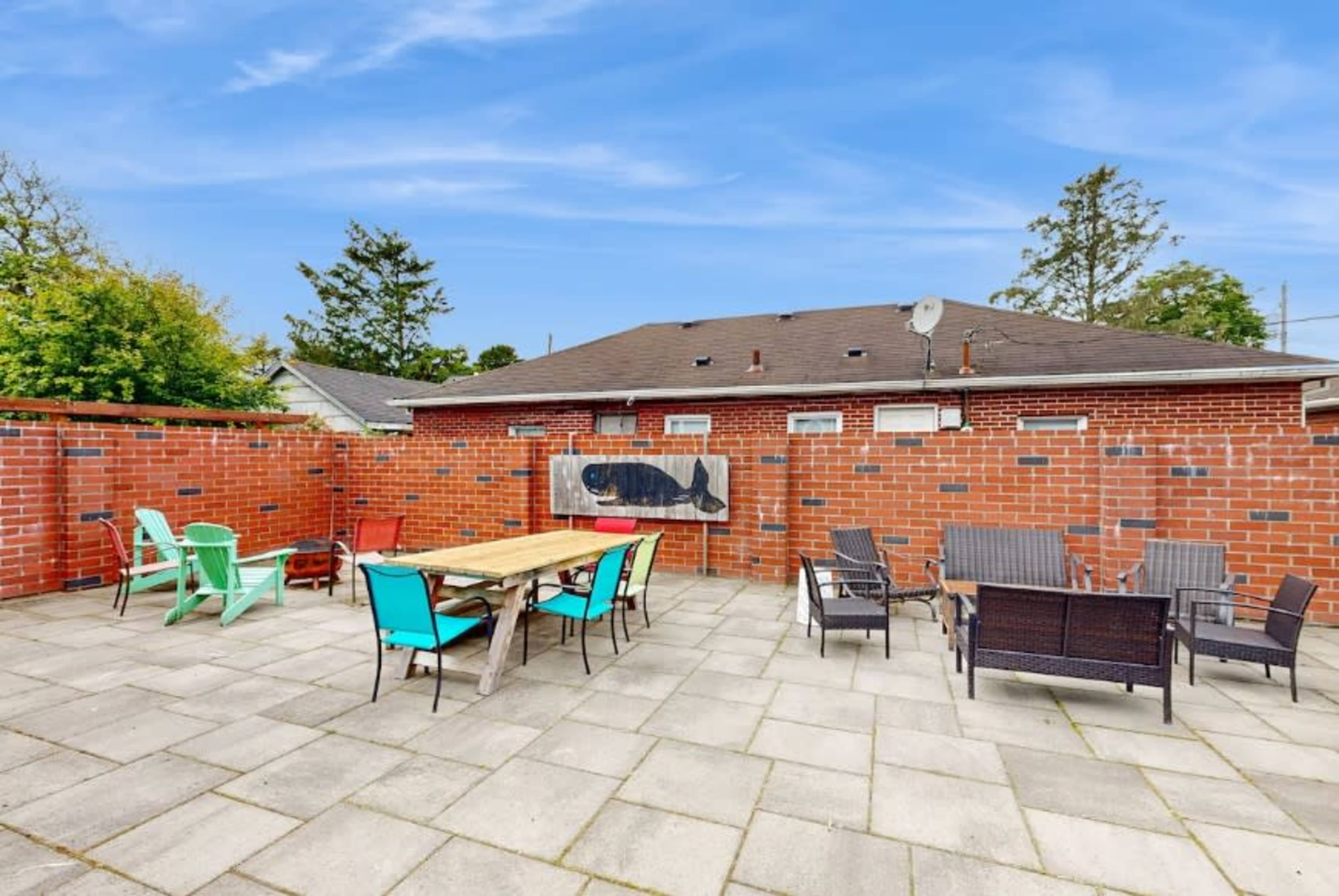 The image shows a spacious outdoor patio area with various seating arrangements, including colorful chairs and a wooden table, surrounded by a brick wall.
