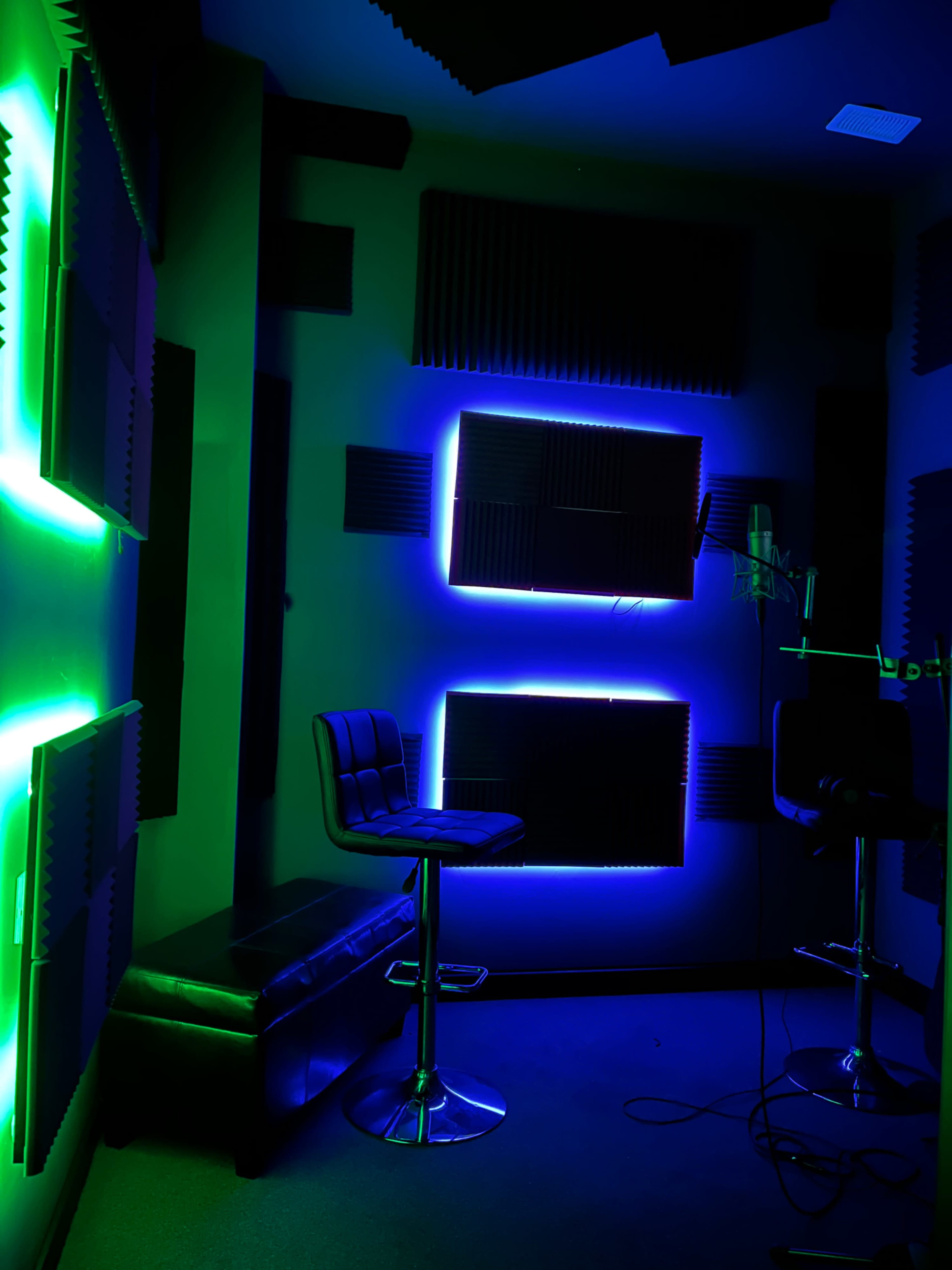 A soundproof recording studio featuring neon green and blue lights, a microphone, and a leather bar stool.
