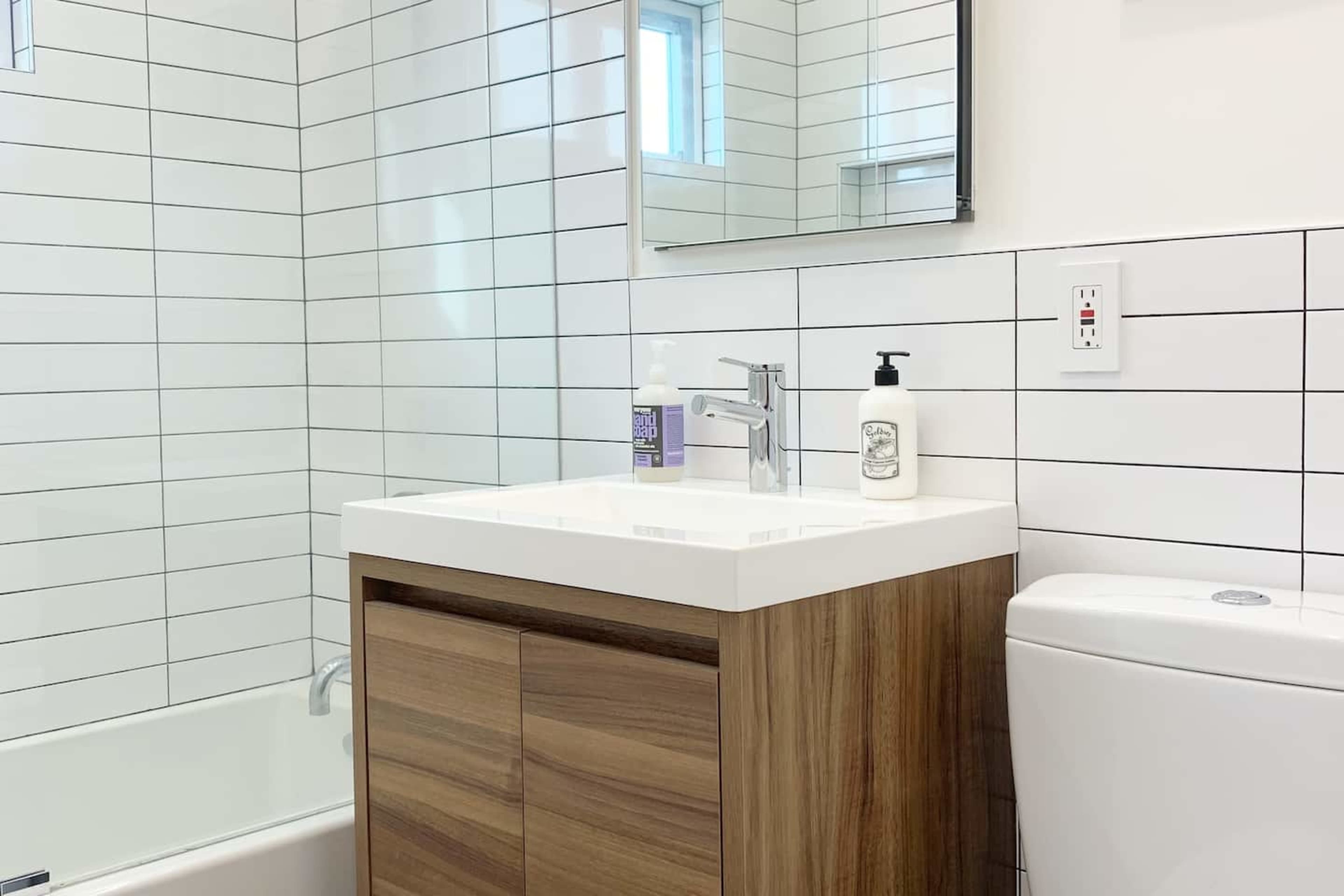 A modern bathroom with a wooden vanity, a white sink, and tiled walls featuring a mirror above the sink.