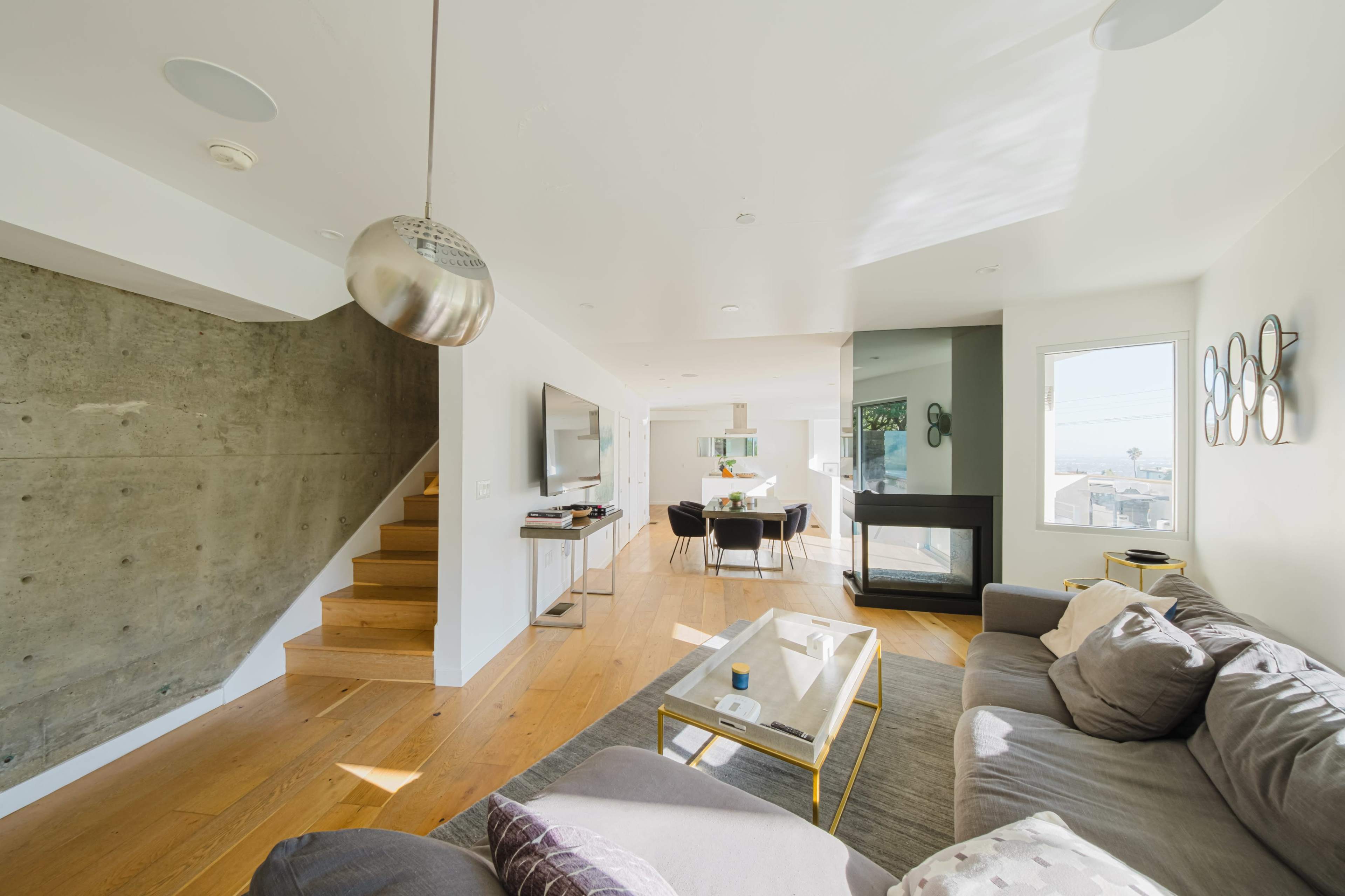 A spacious living area features a gray sofa, a glass coffee table, and a staircase leading to an upper level.