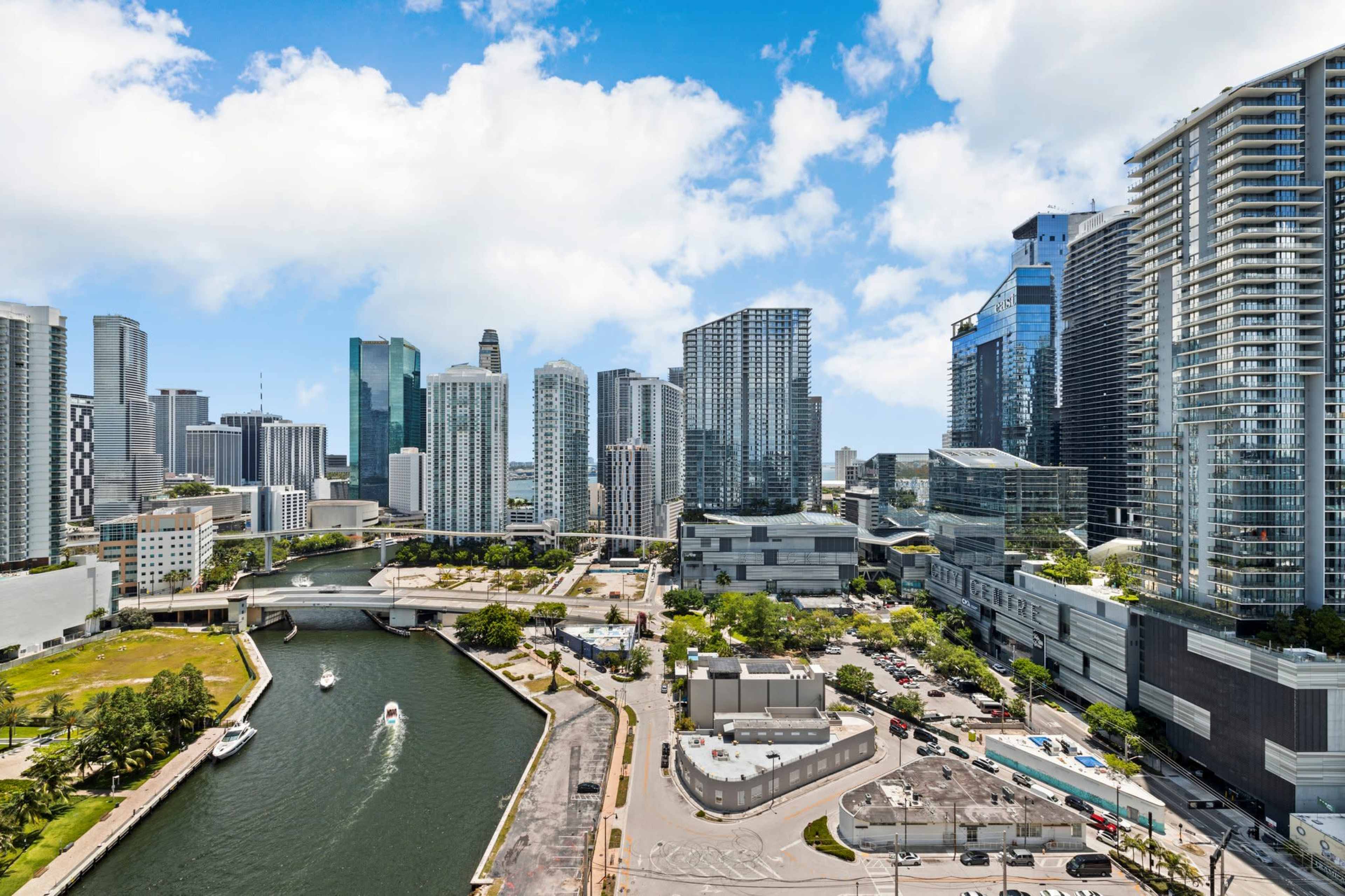 A panoramic view of a modern urban skyline with high-rise buildings along a waterfront and a busy canal in the foreground.