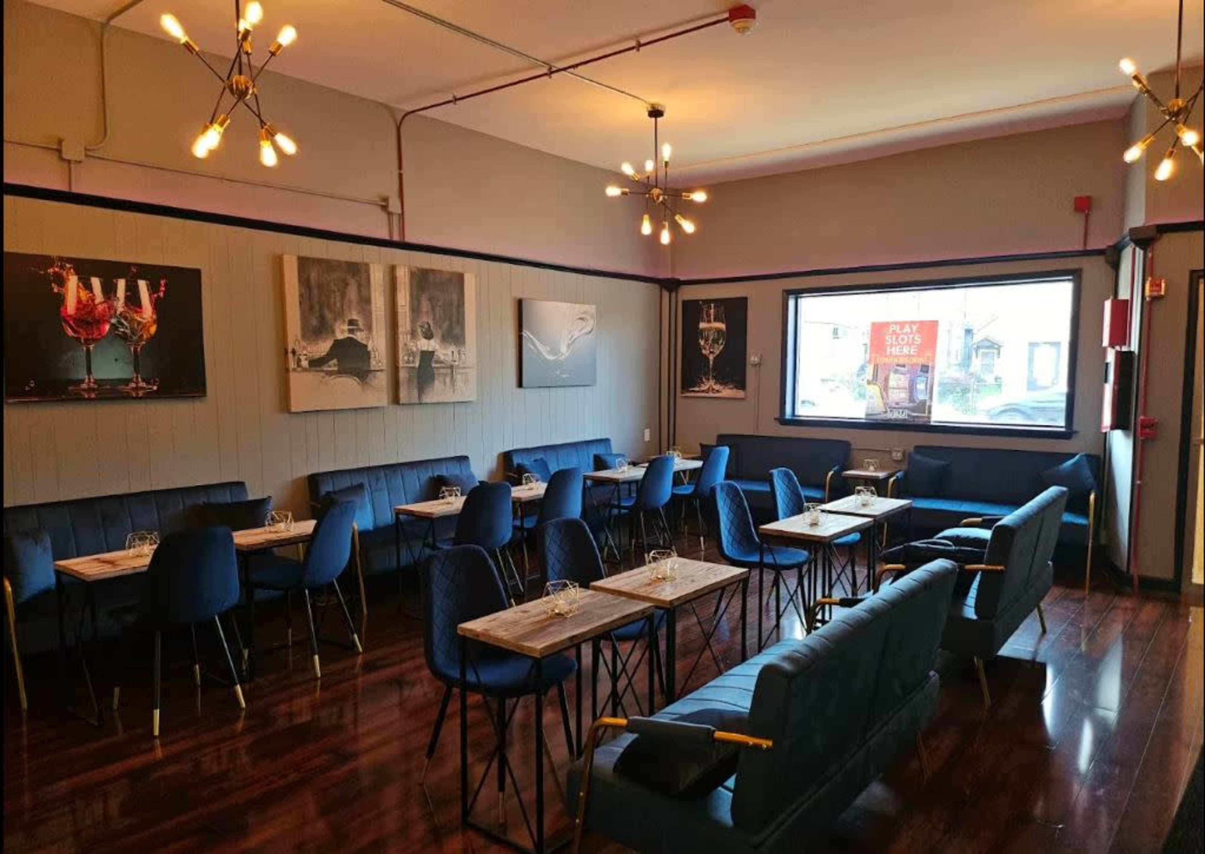 The image shows a modern restaurant interior with wooden tables, blue seating, and artistic wall decor featuring images of drinks.