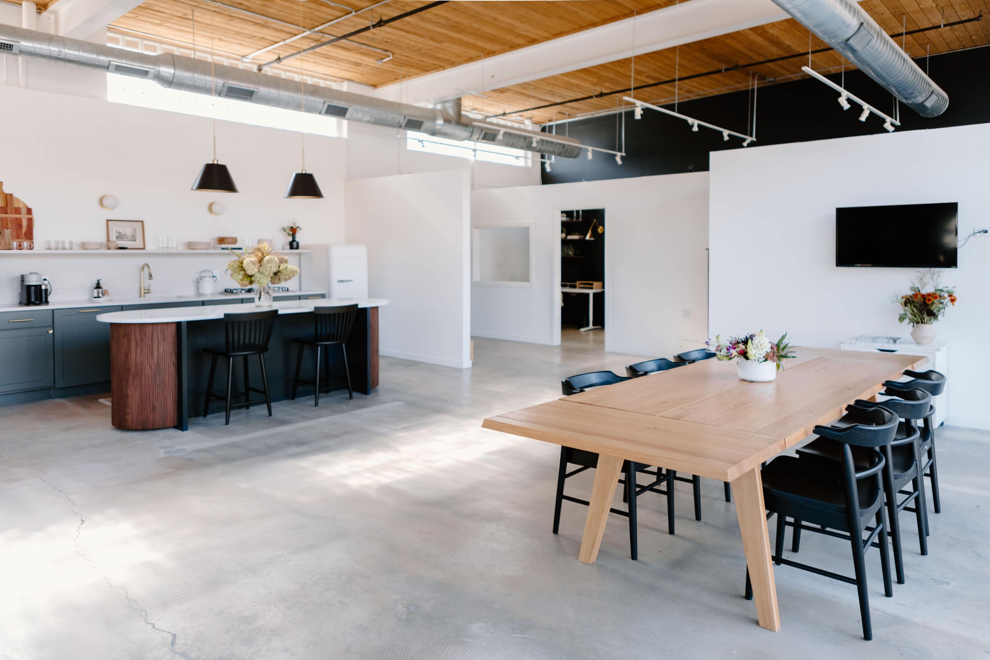 A modern kitchen and dining area features an open layout with a large wooden table, black chairs, and a well-equipped kitchen.