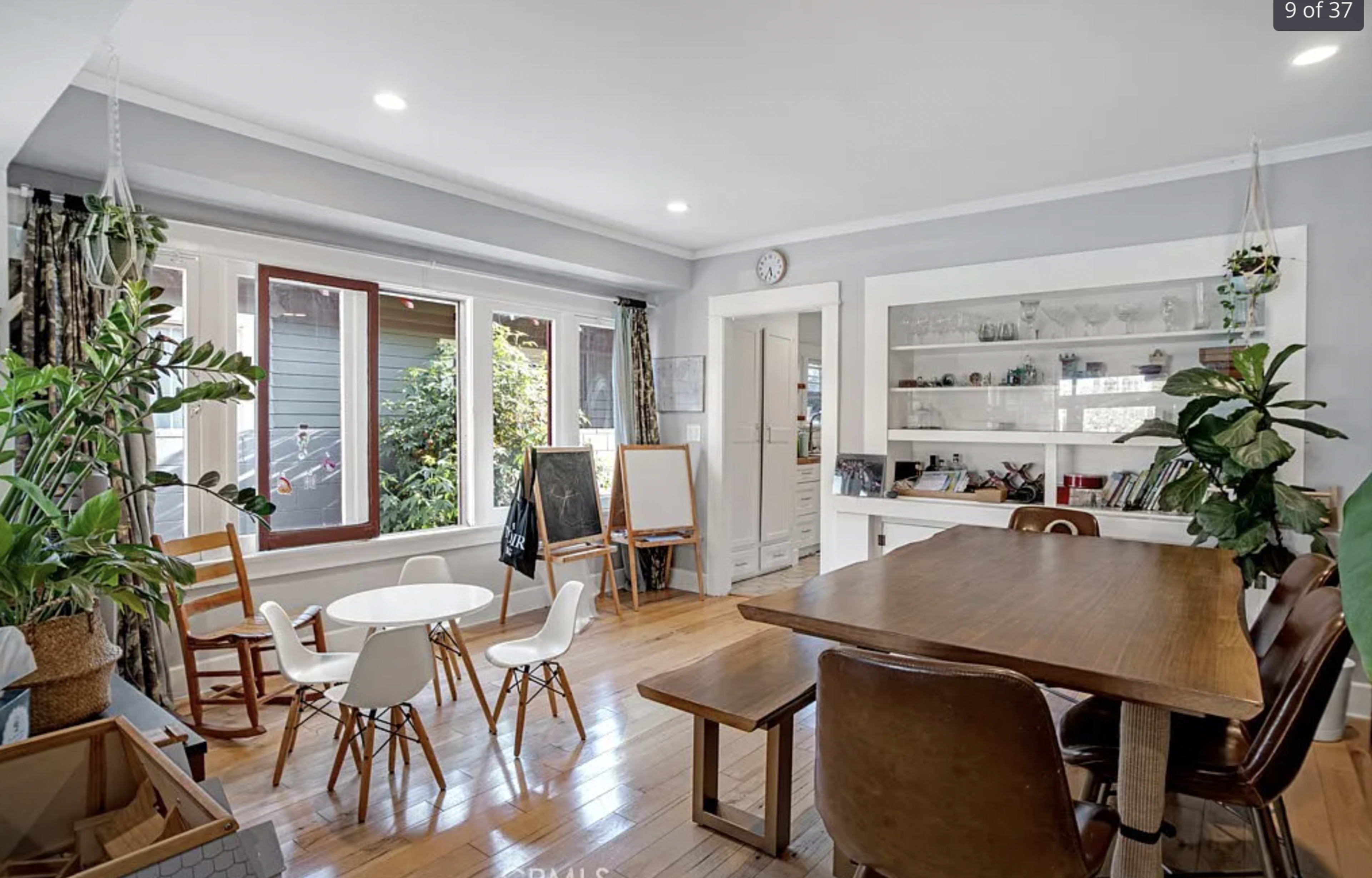 A bright dining area features a wooden table, white chairs, and a large window, enhancing the open atmosphere.