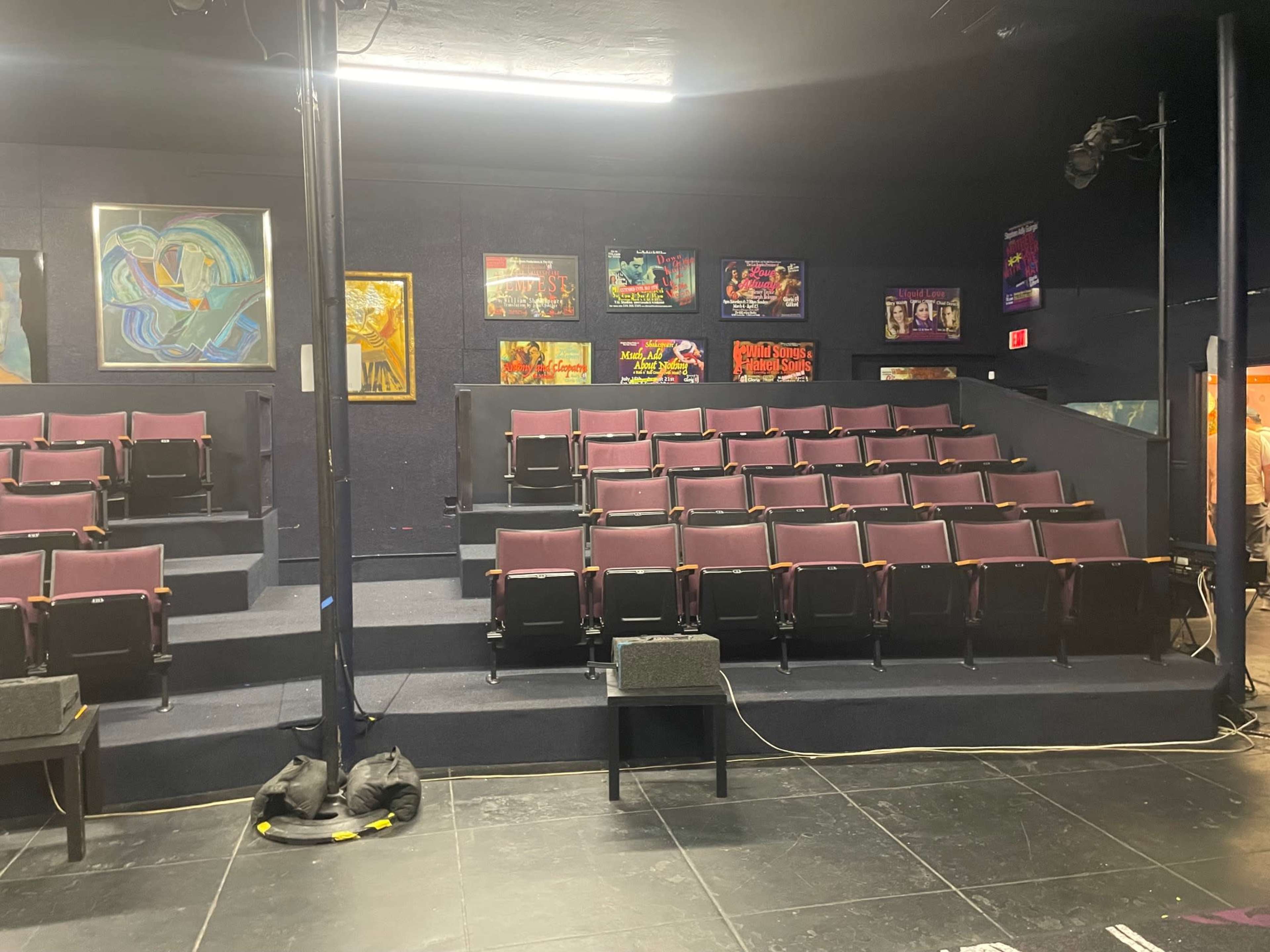 An empty theater space with tiered seating, black walls, and colorful artwork displayed on the back wall.