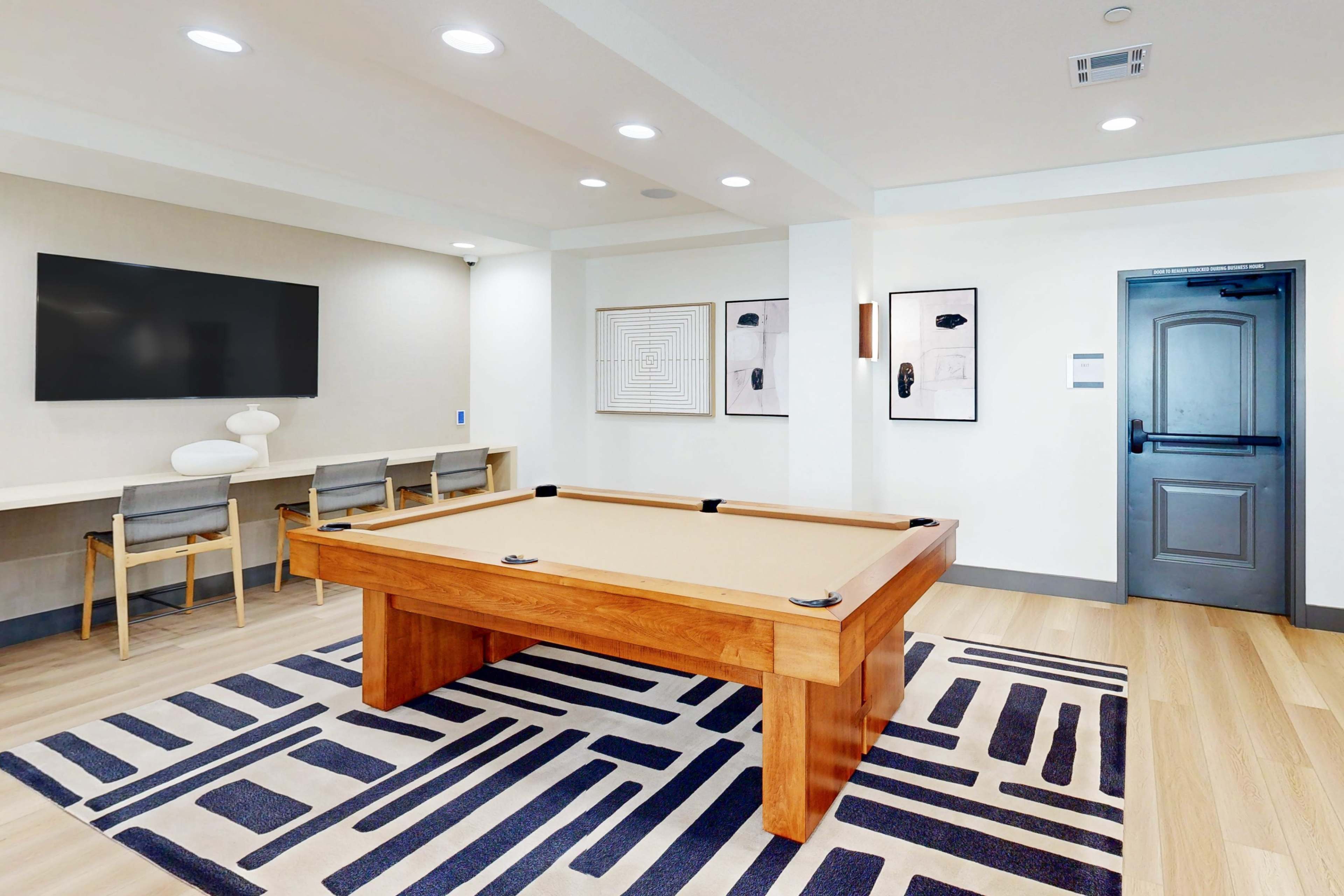 The image shows a room with a pool table, a large TV mounted on the wall, and a seating area with several chairs.
