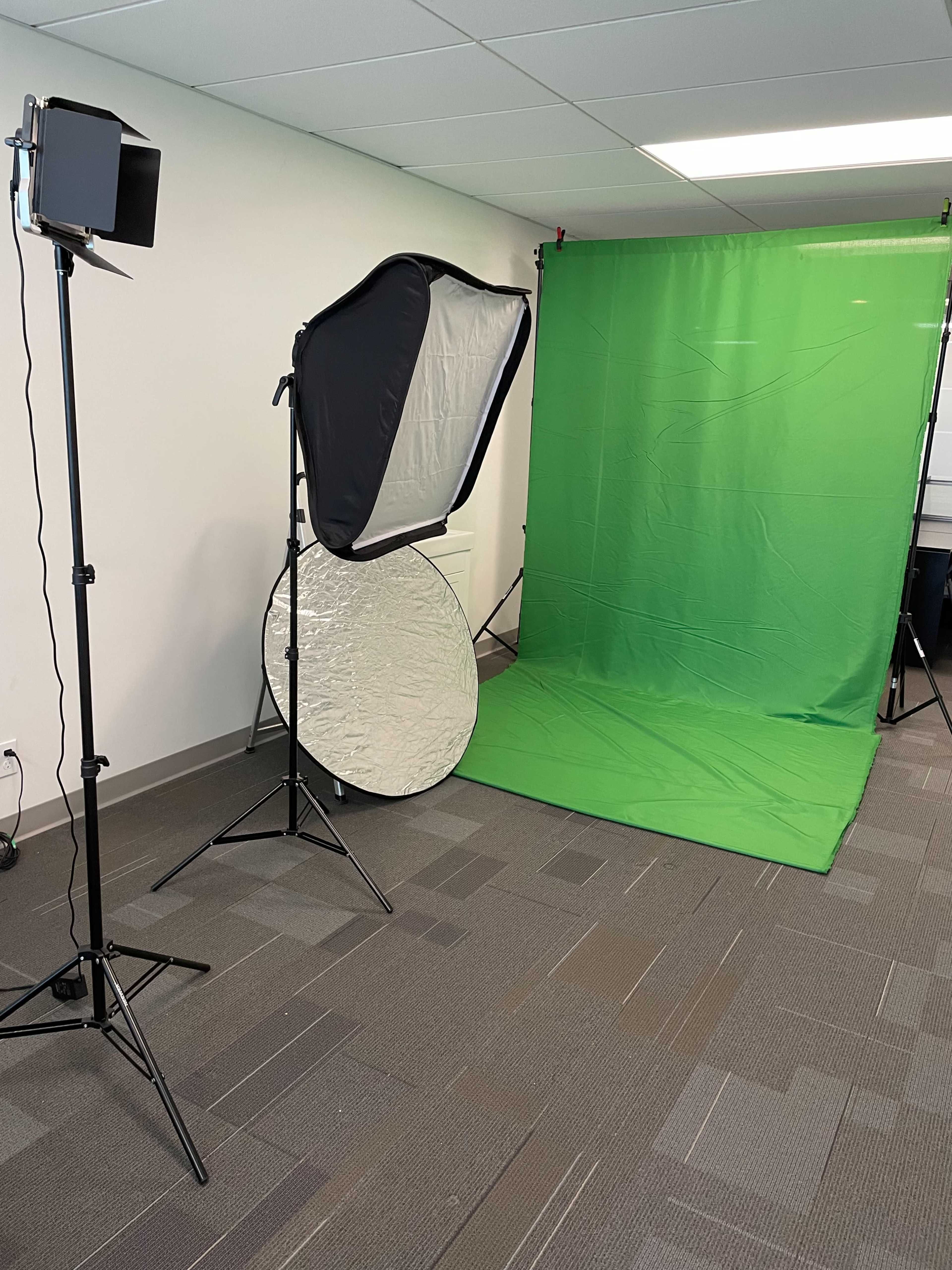 A green screen setup in an indoor space, featuring a light stand, softbox, and a reflector.