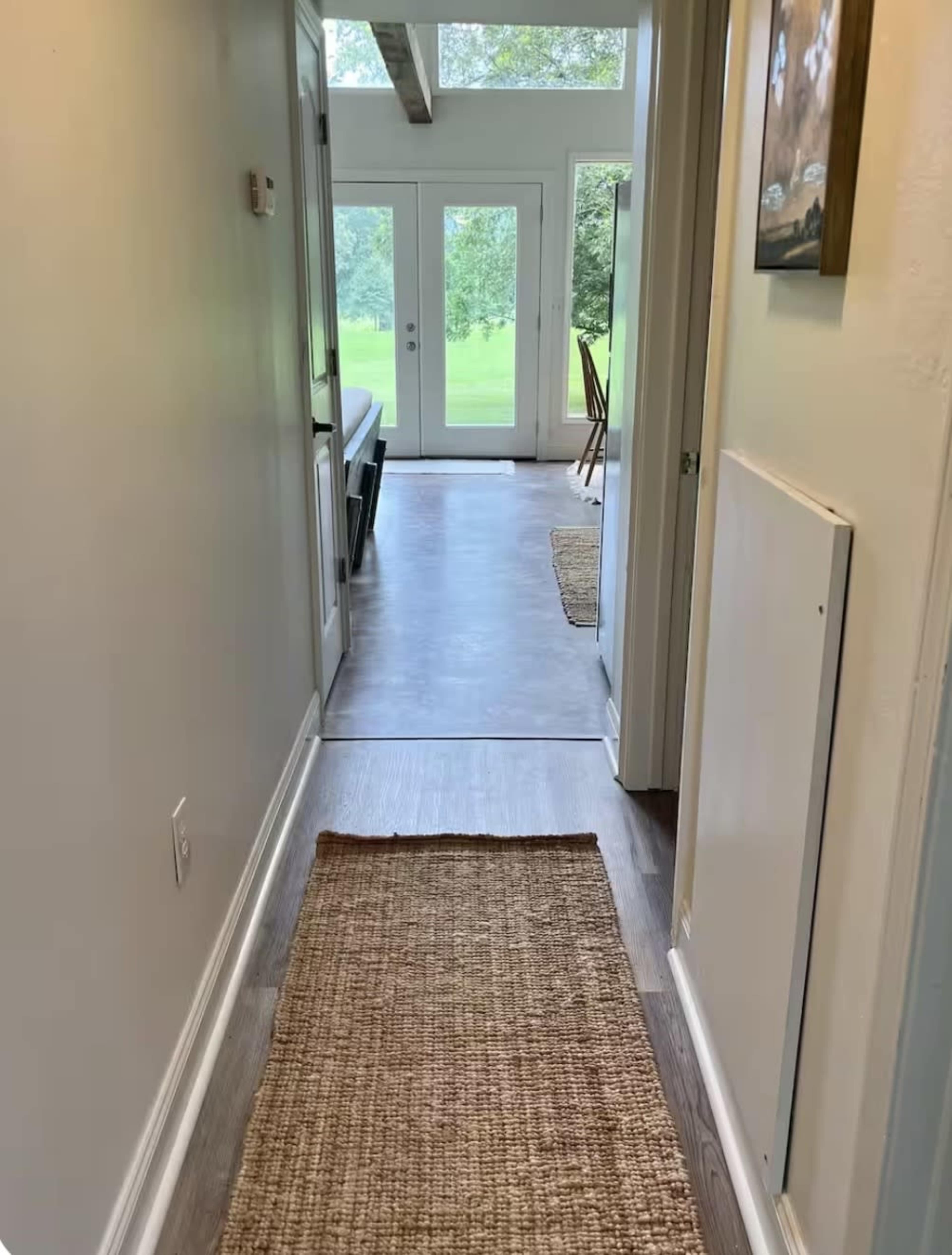 A narrow hallway leads to a set of glass doors that open to a grassy outdoor area.