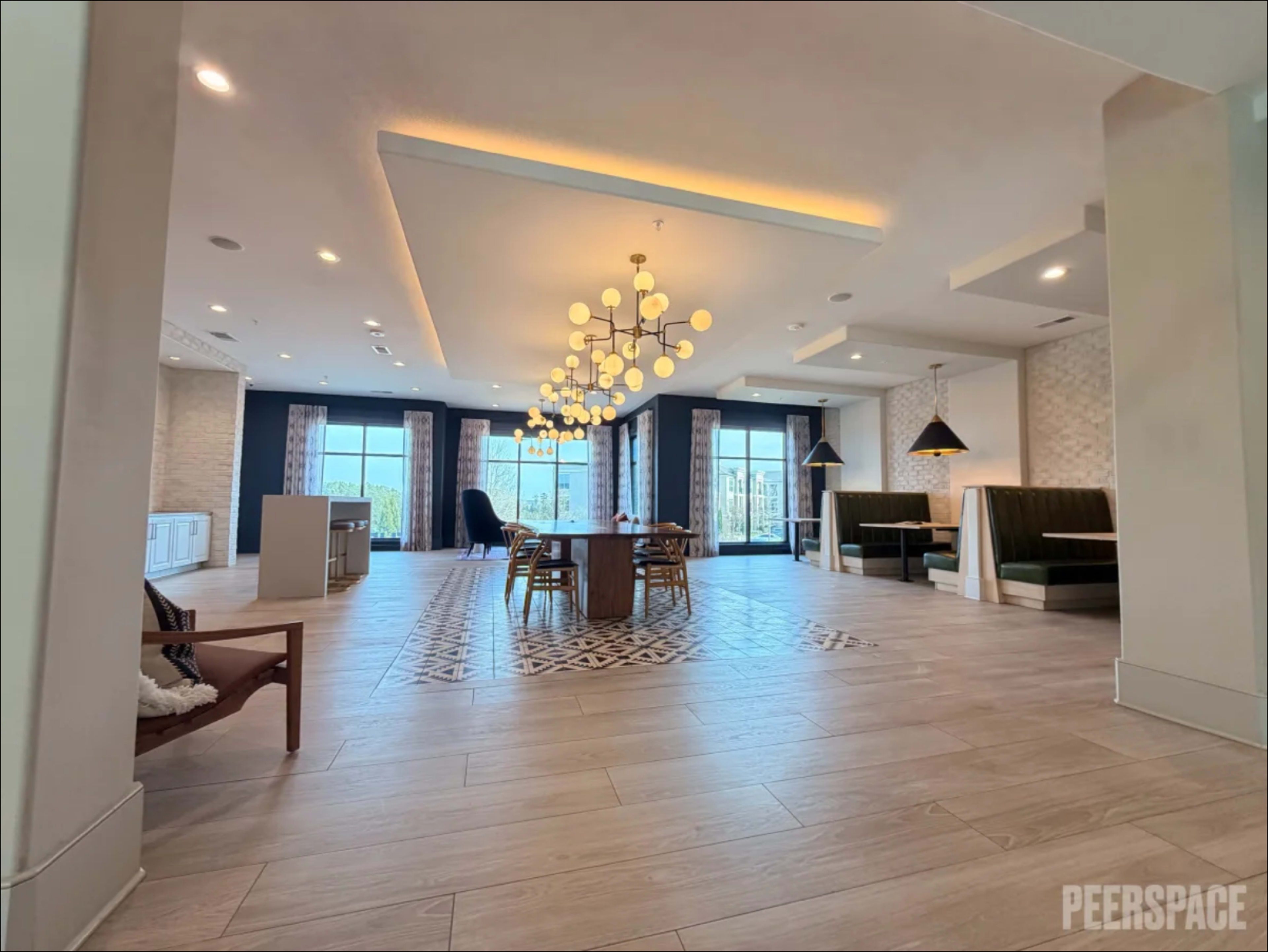 The image shows a spacious, well-lit lobby area with a dining table, modern lighting fixtures, and seating arrangements.