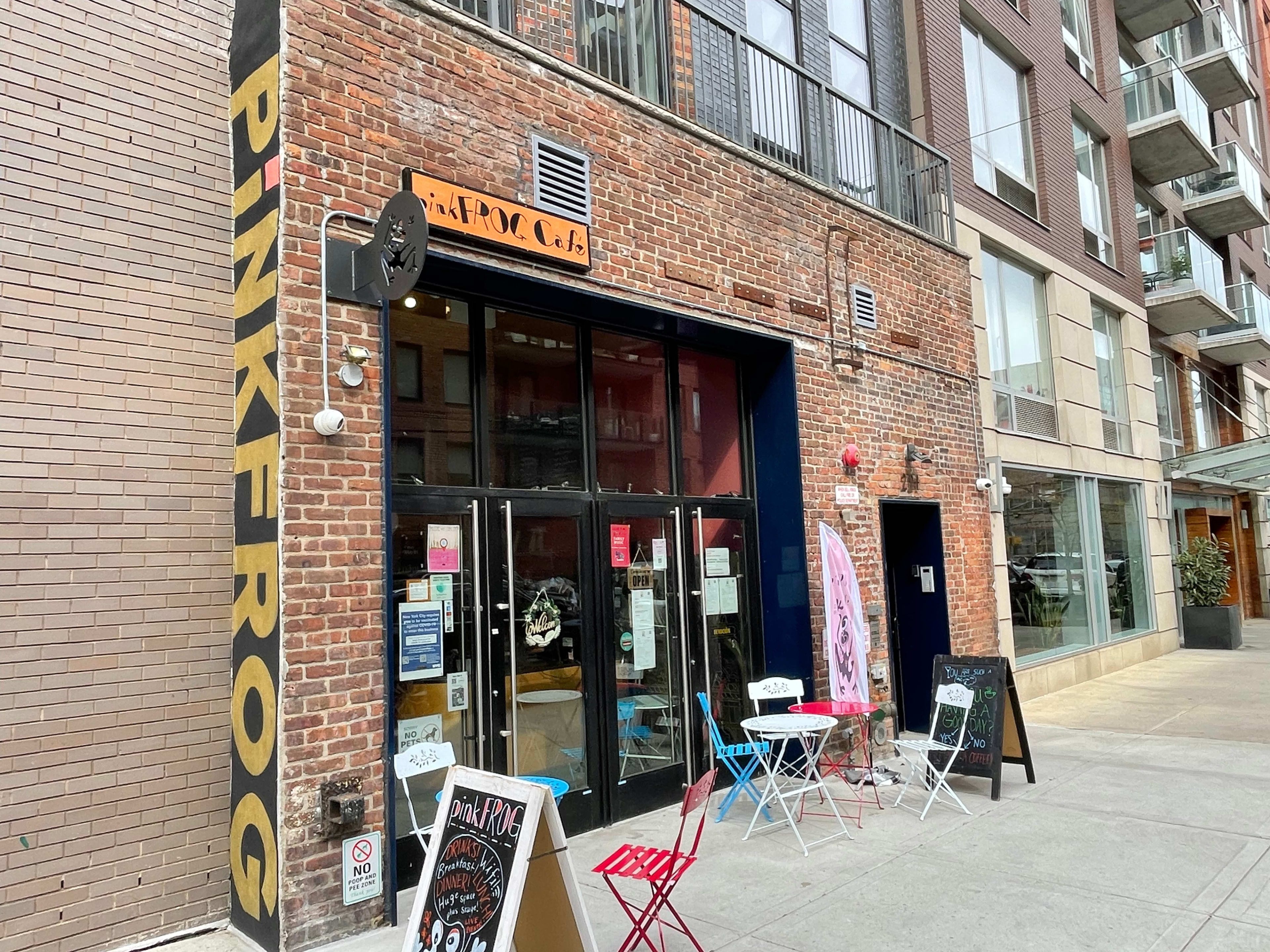A brick storefront labeled "PINK FROG" with large glass doors and outdoor seating on a city sidewalk.
