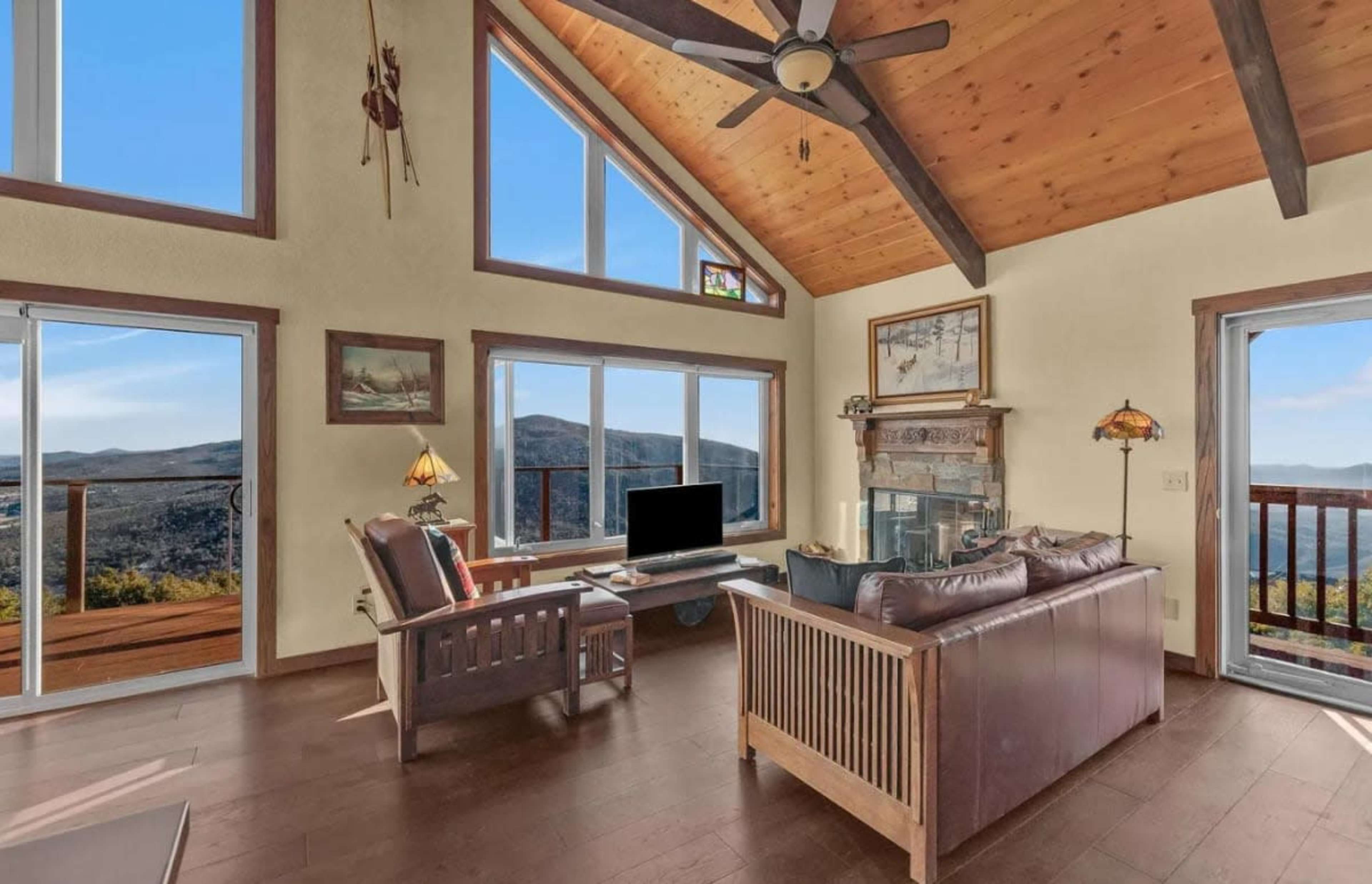 The image shows a modern living room with large windows, a wooden ceiling, and a view of mountains outside.