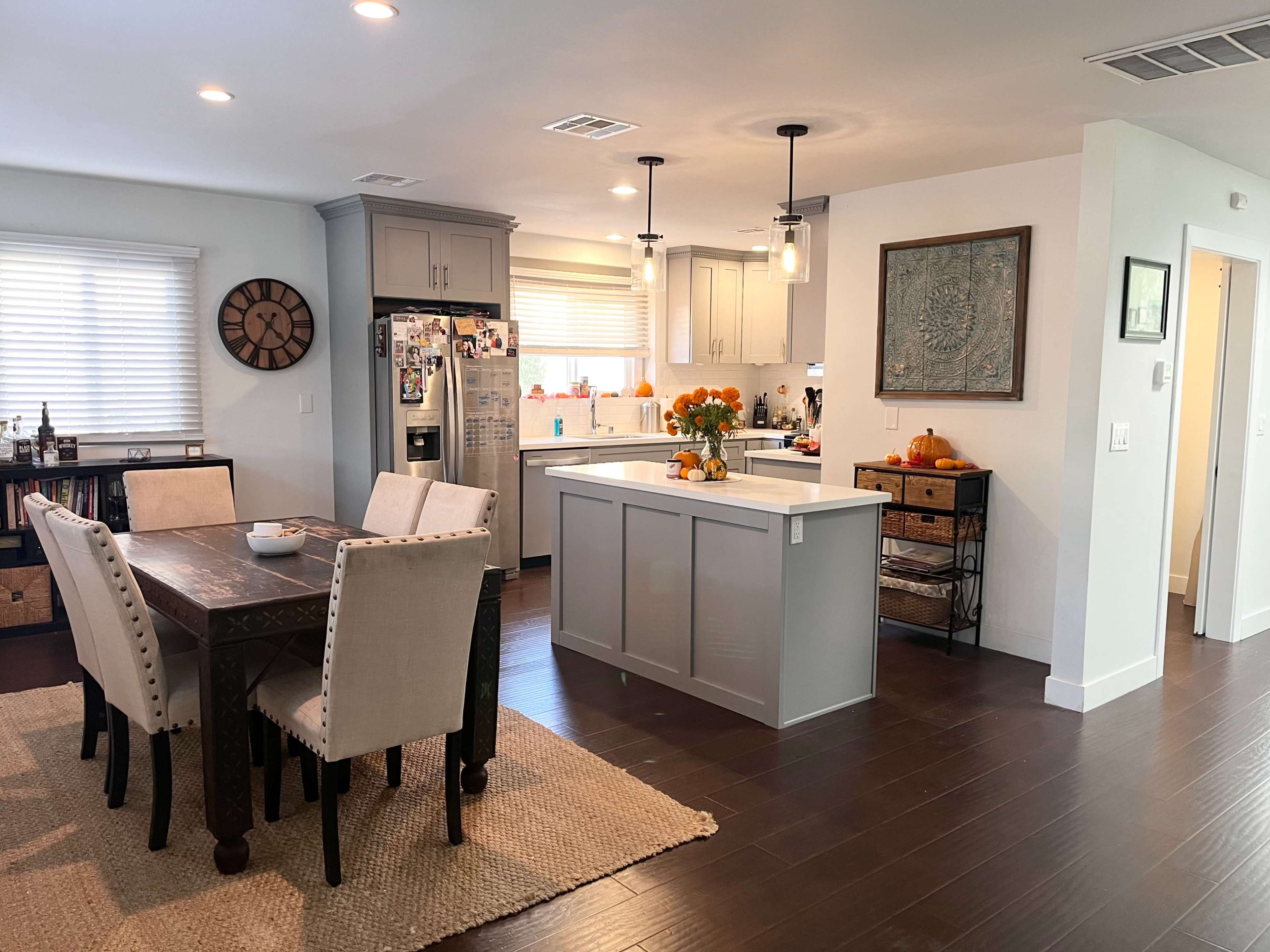 A modern kitchen and dining area feature a central island with bar seating, a wooden dining table, and an organized space with warm lighting.