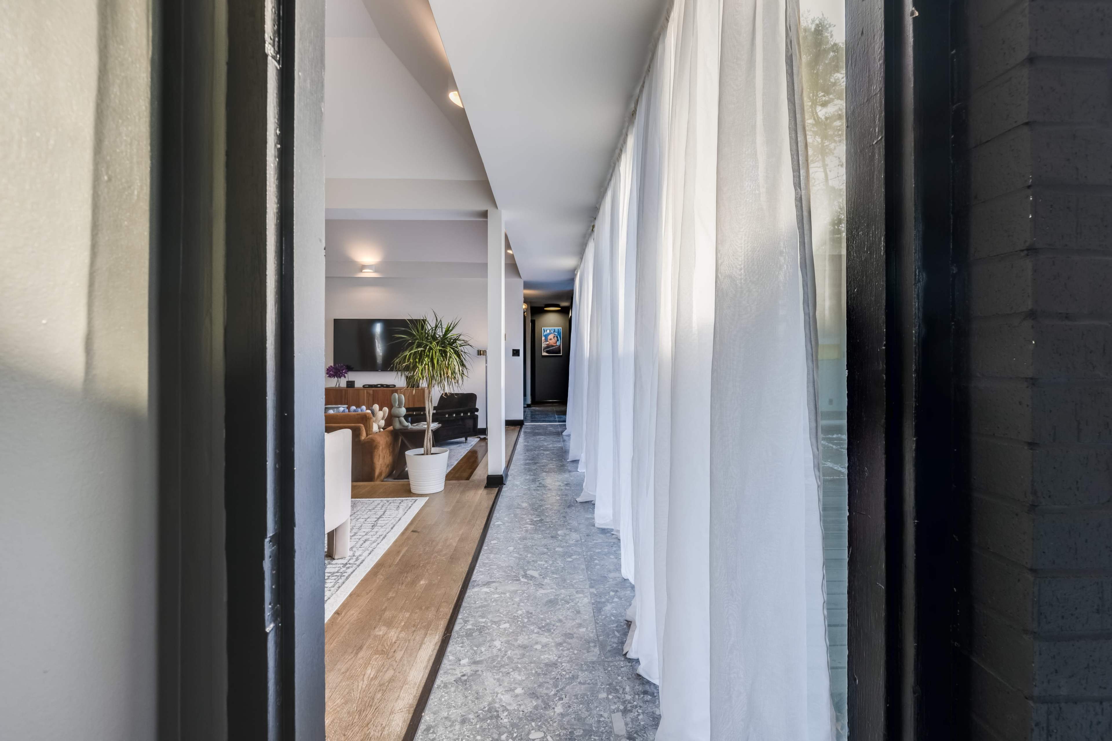A hallway leading to a living area, lined with sheer white curtains and featuring a patterned floor.