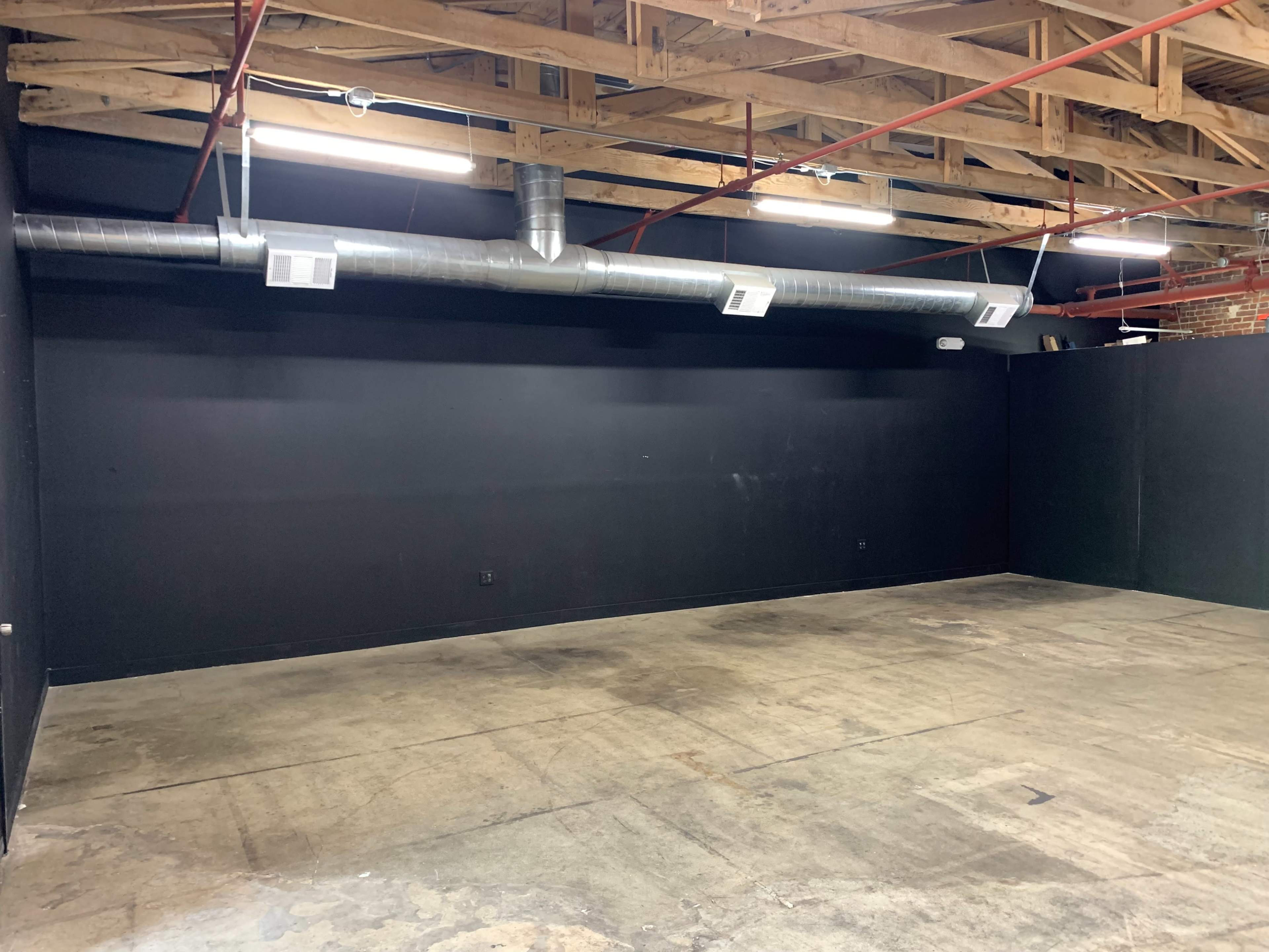 A spacious, empty room with black walls and exposed wooden beams in the ceiling.