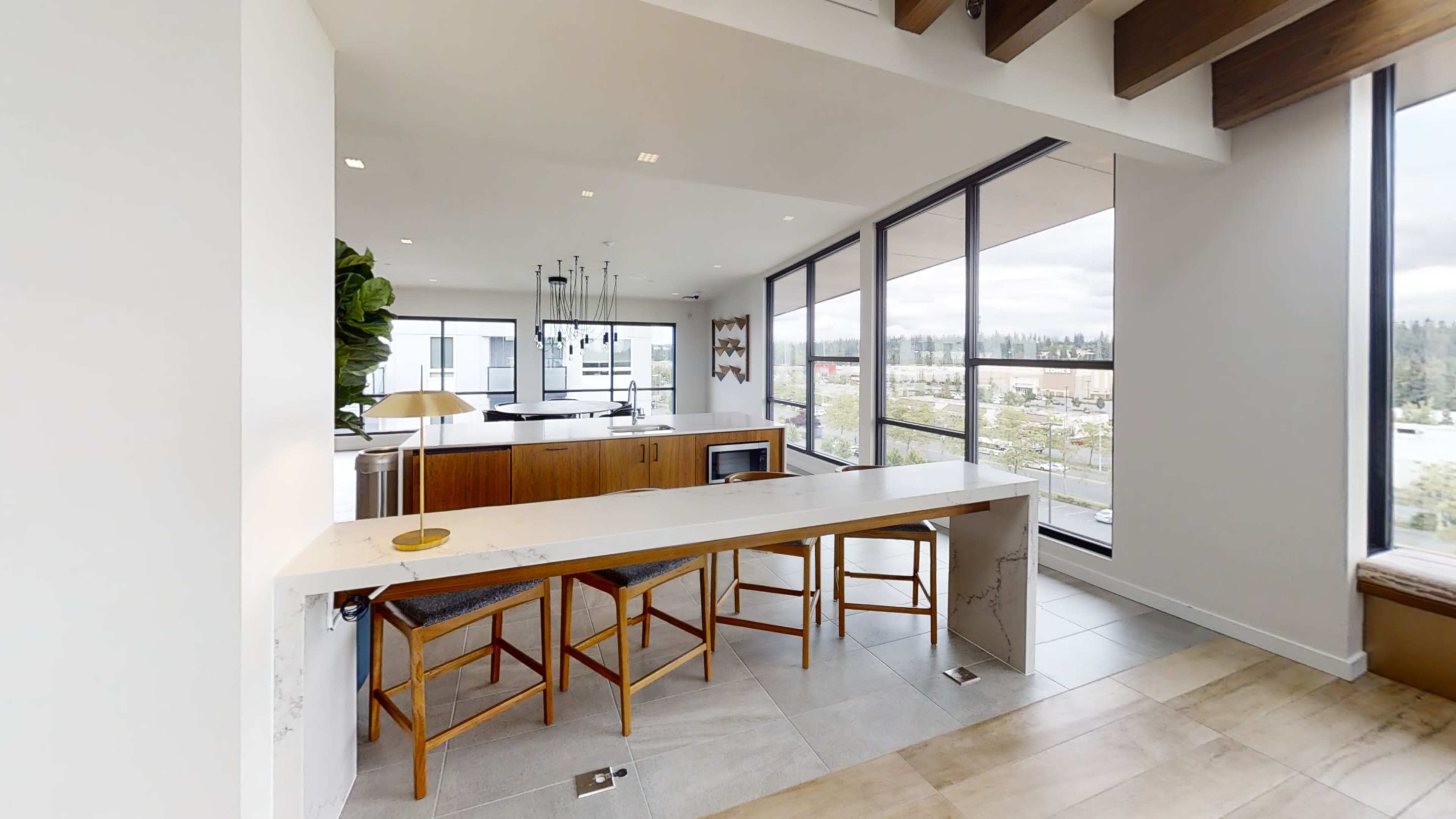 A modern kitchen with a countertop and three wooden stools, featuring large windows that provide a view of the exterior landscape.