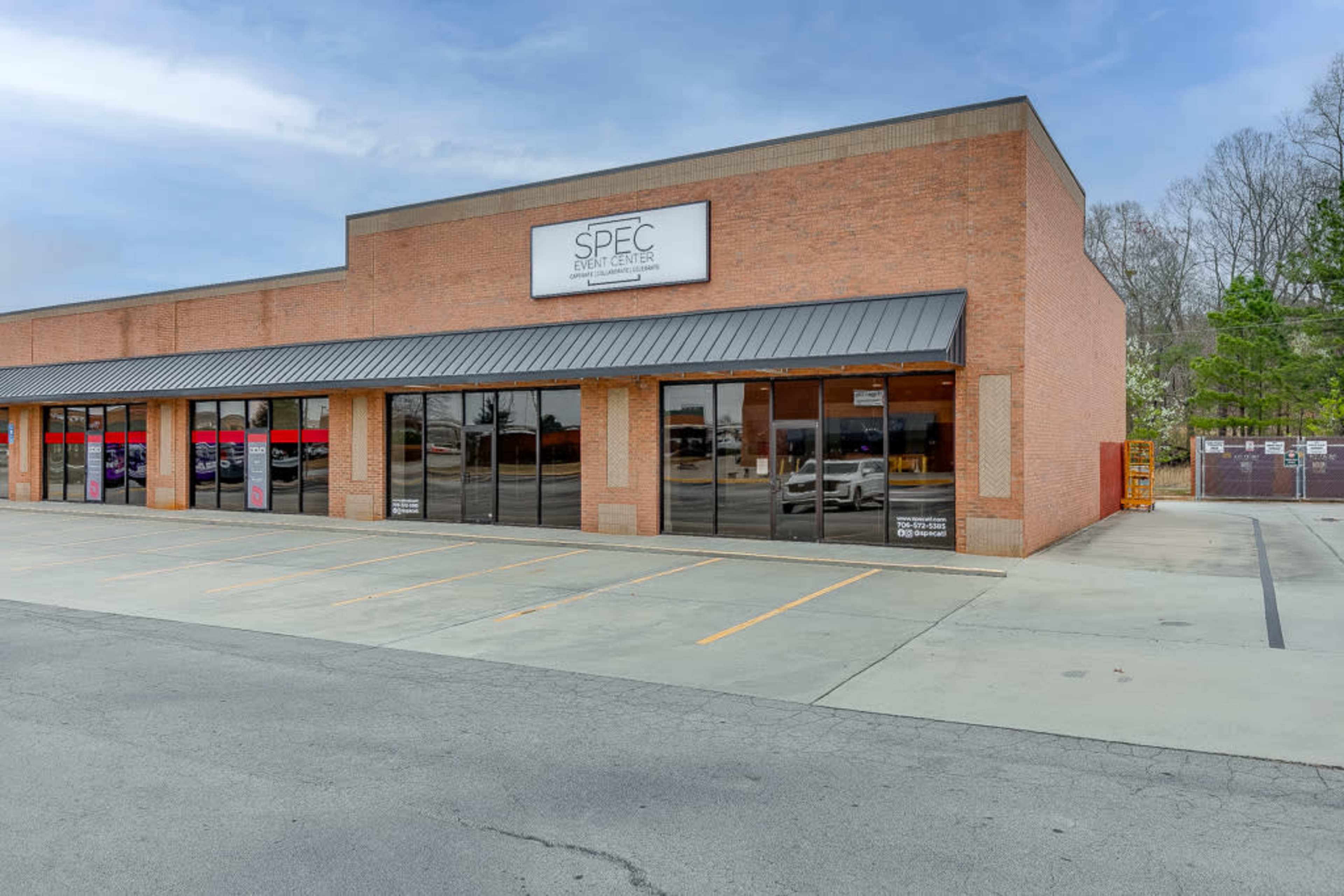 A brick building with large glass windows and a sign reading "SPEC Event Designs" is situated in a parking lot.