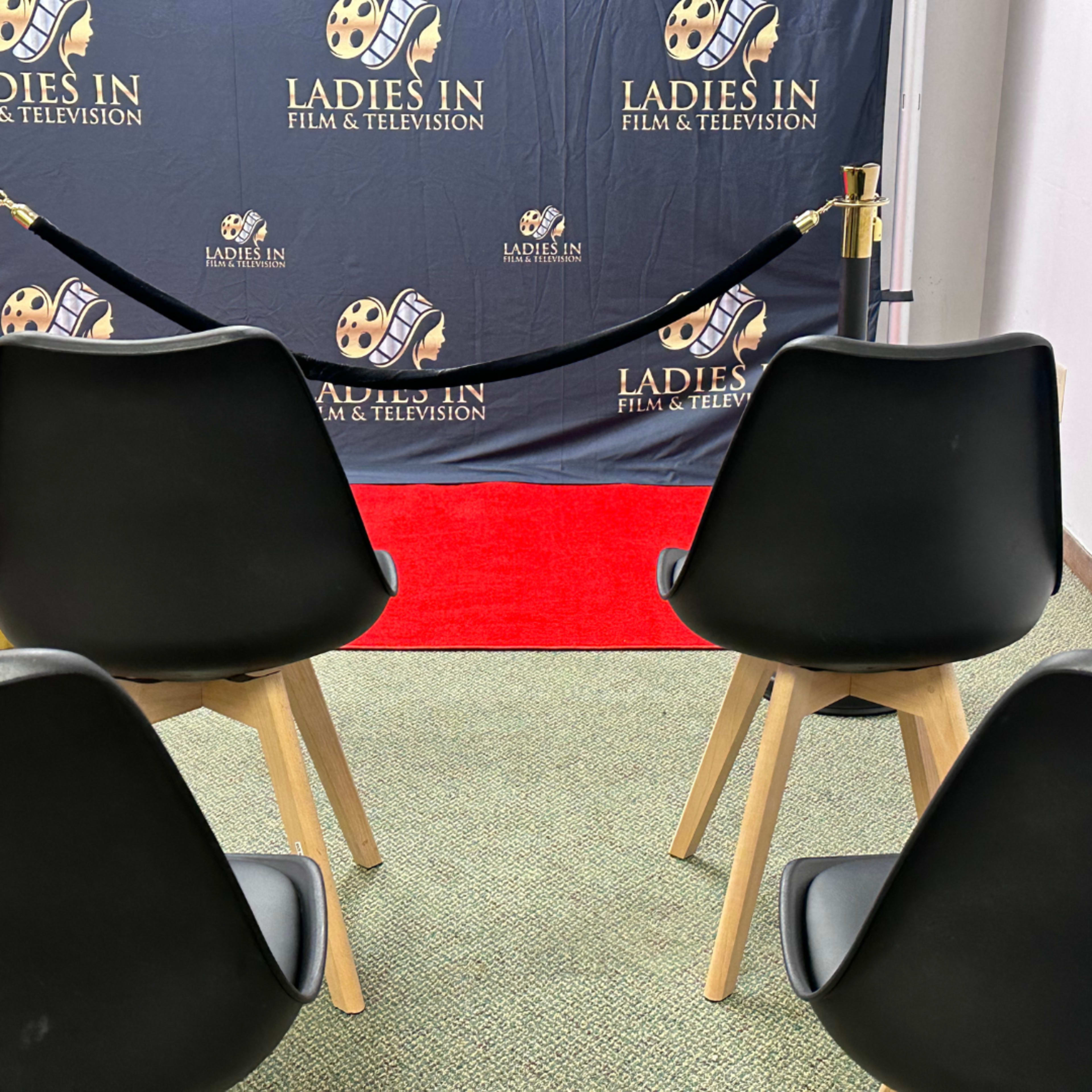 A red carpet area with black chairs arranged in front of a backdrop featuring the text "Ladies in Film & Television."