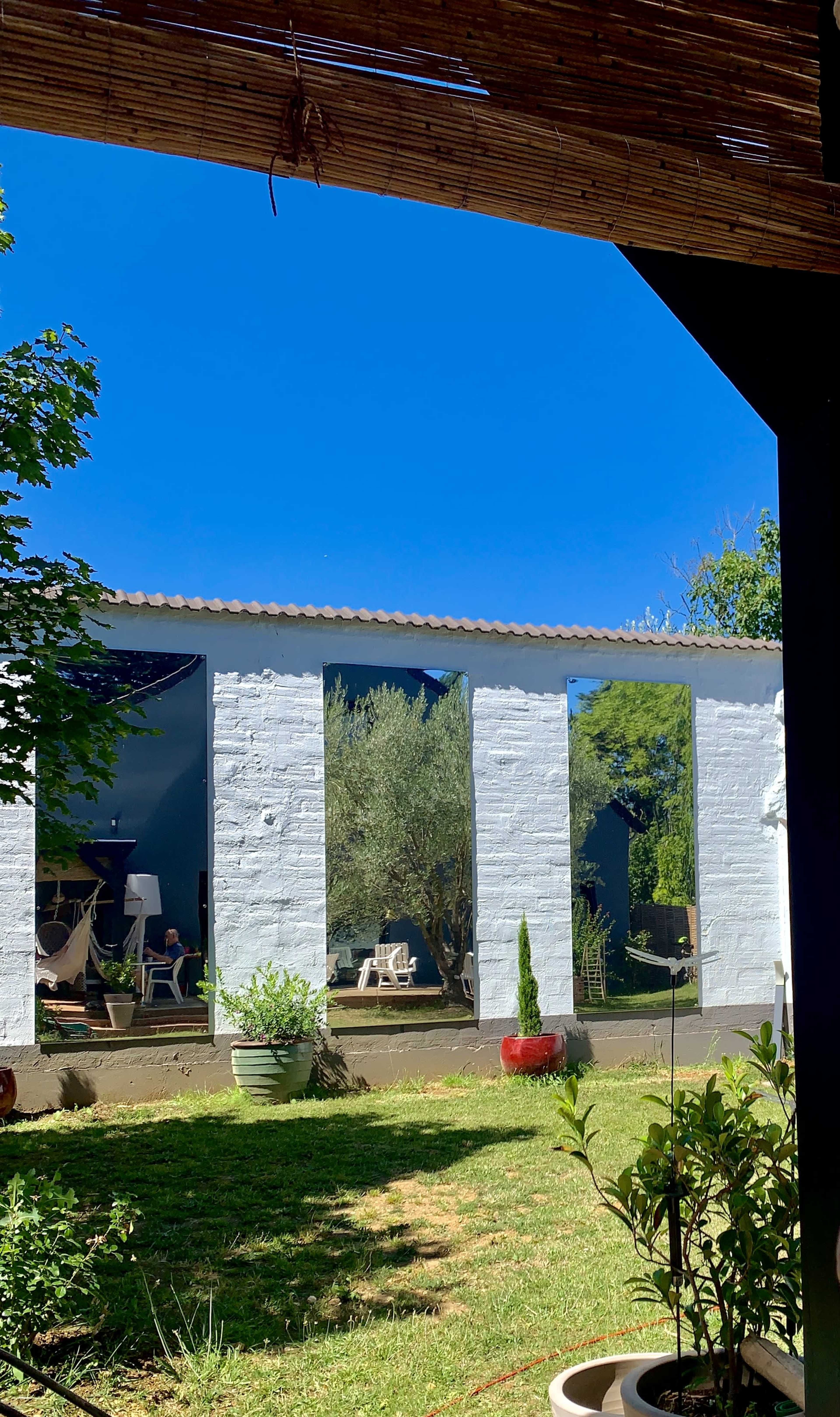 A white-walled building with large openings, surrounded by greenery and potted plants under a clear blue sky.