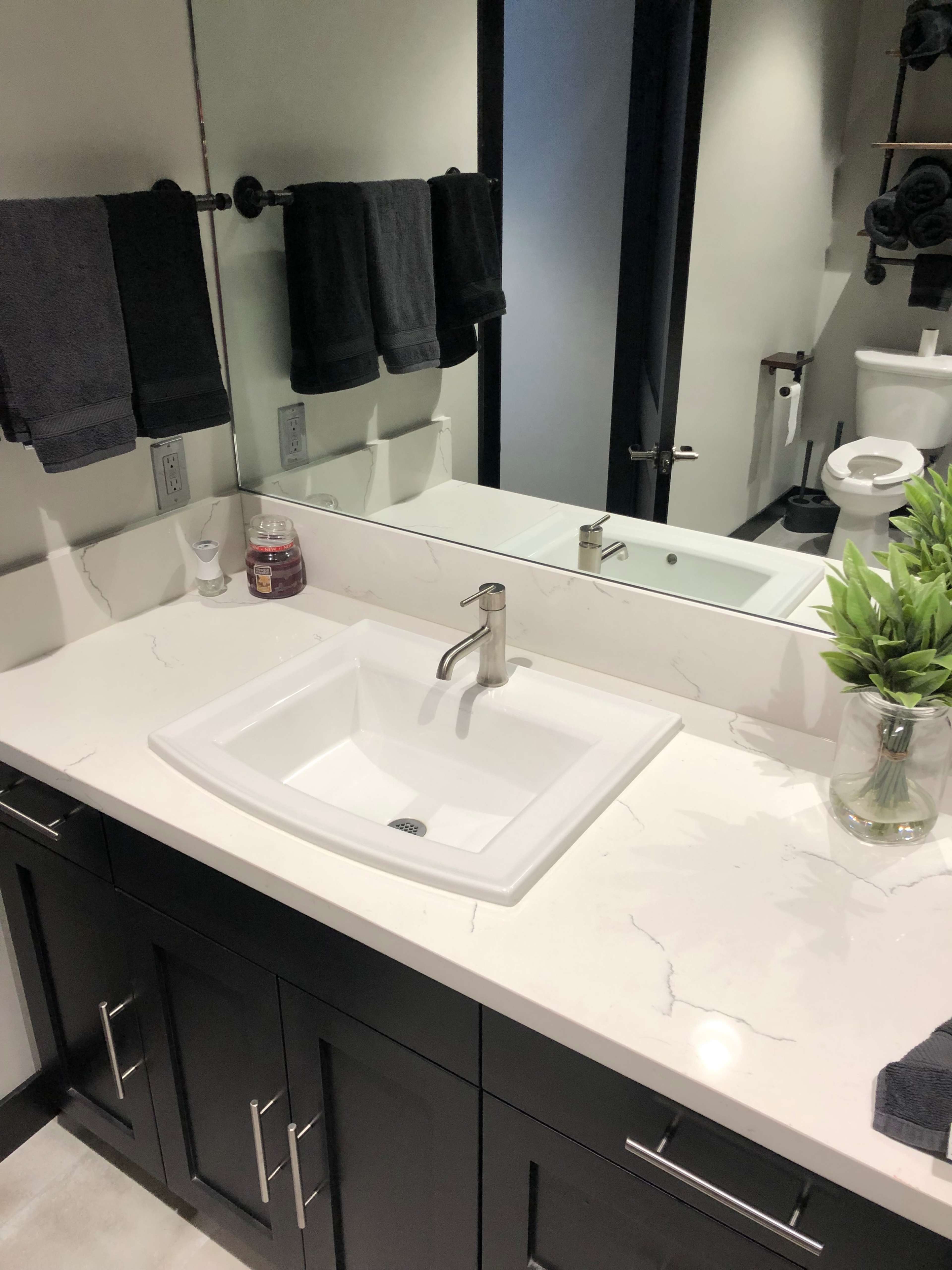 A modern bathroom sink area featuring a white sink, dark cabinetry, a mirror, and neatly arranged towels.