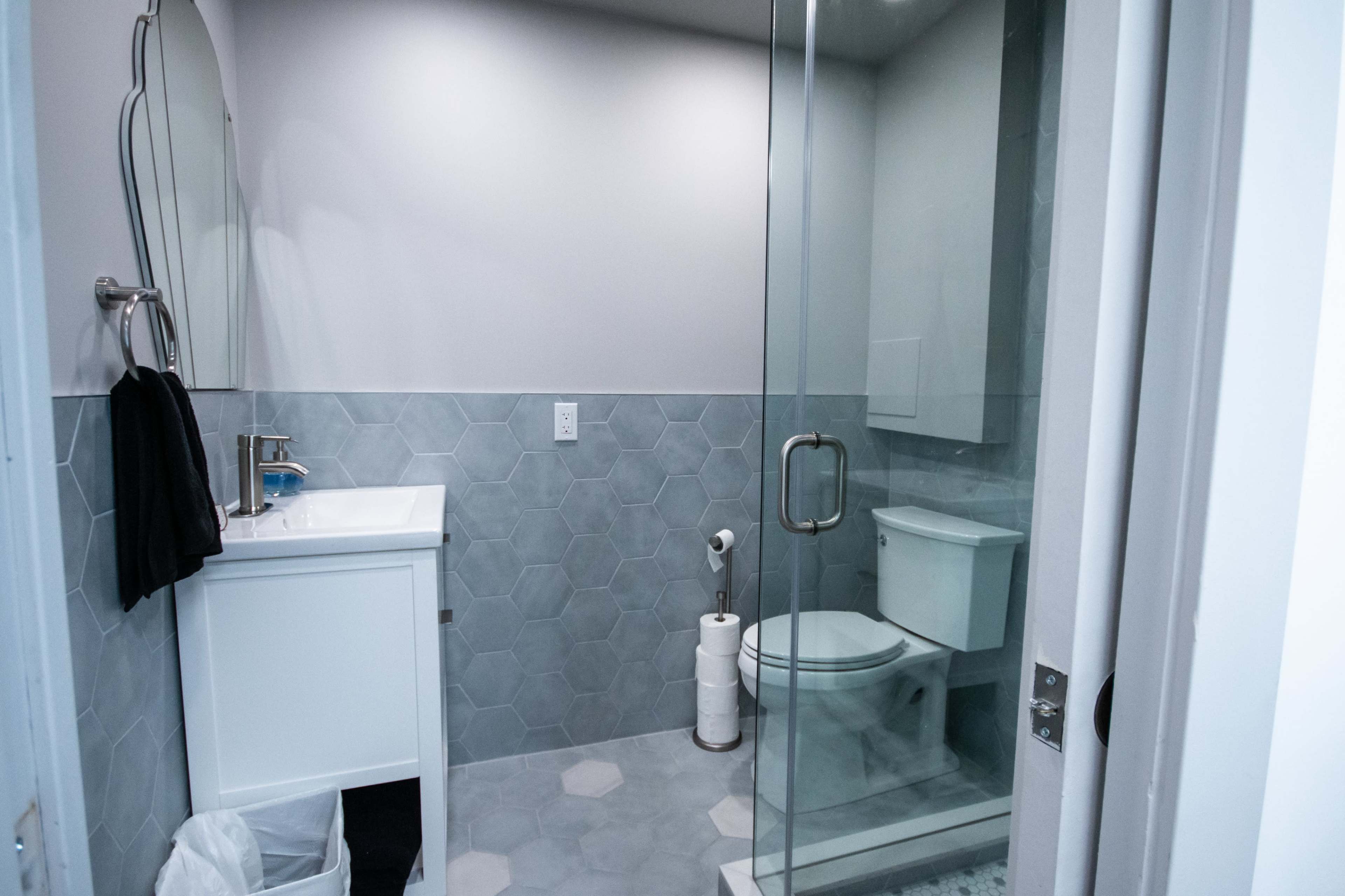 A modern bathroom featuring a glass shower, a white toilet, a sink with a mirror, and hexagonal tiled flooring.
