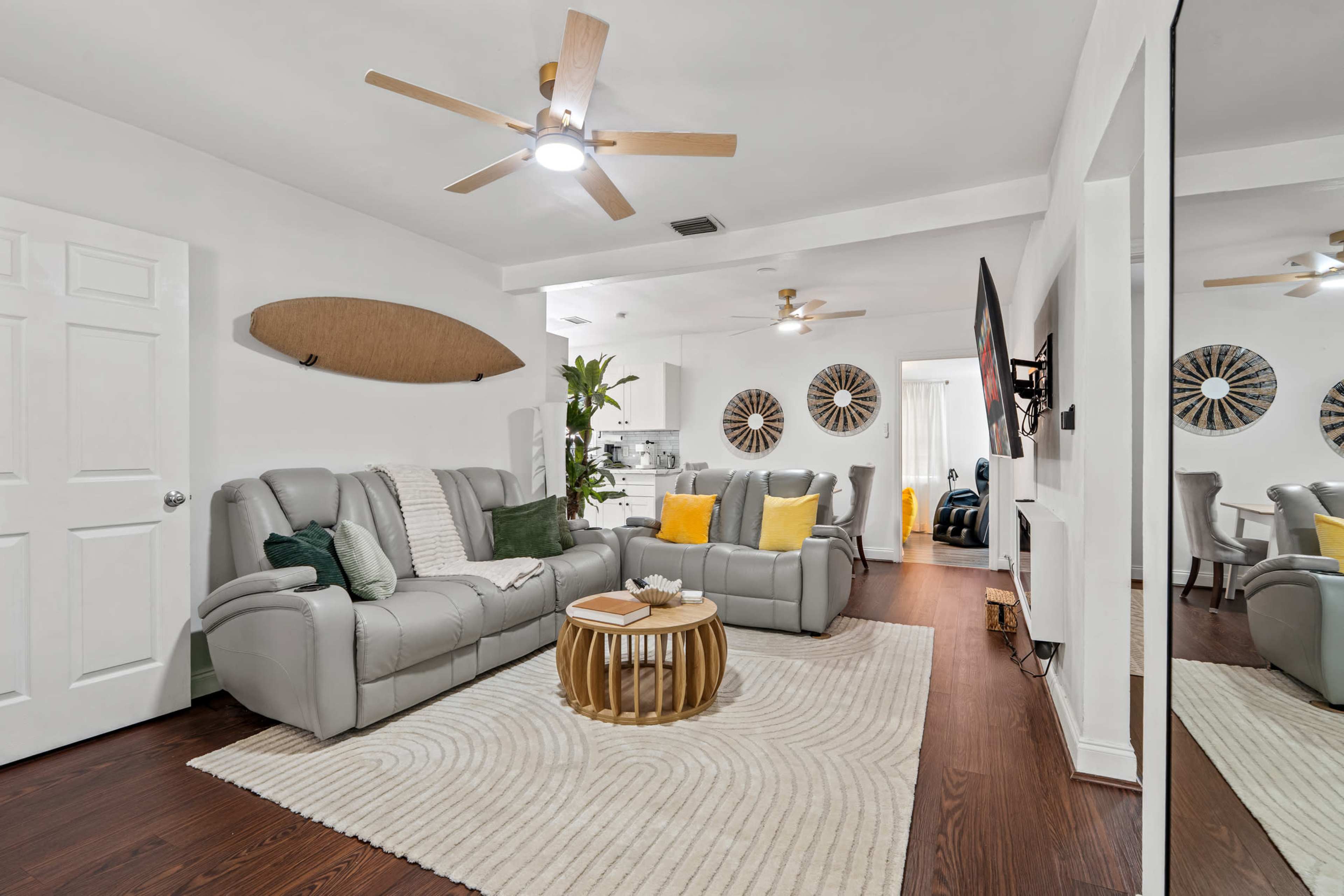 The living room features a light-colored sofa set, a circular coffee table, and a textured area rug, with a dining area visible in the background.