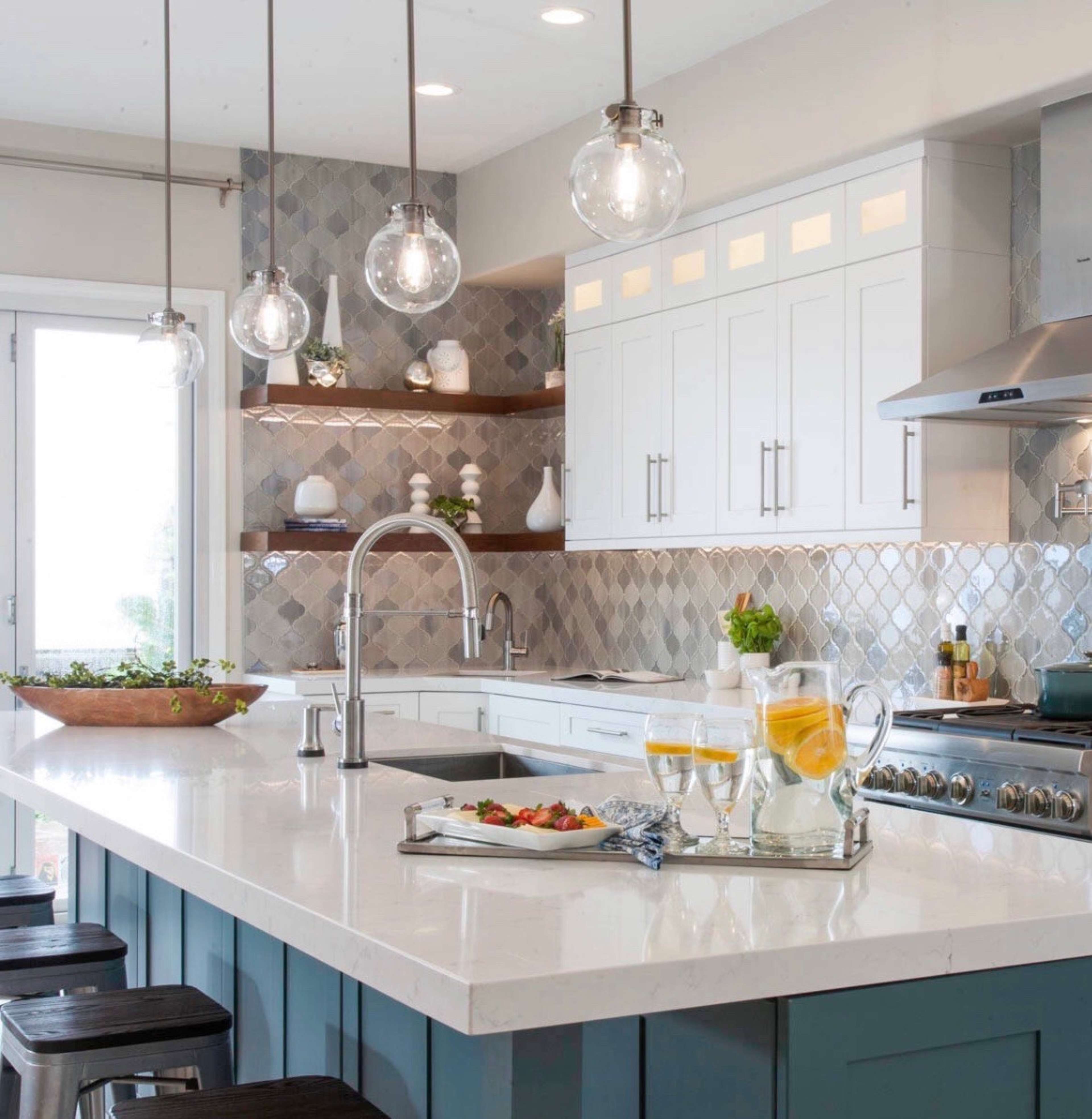 The image features a modern kitchen with a large island, silver pendant lights, and a mix of white and blue cabinetry, accented by a tiled backsplash.