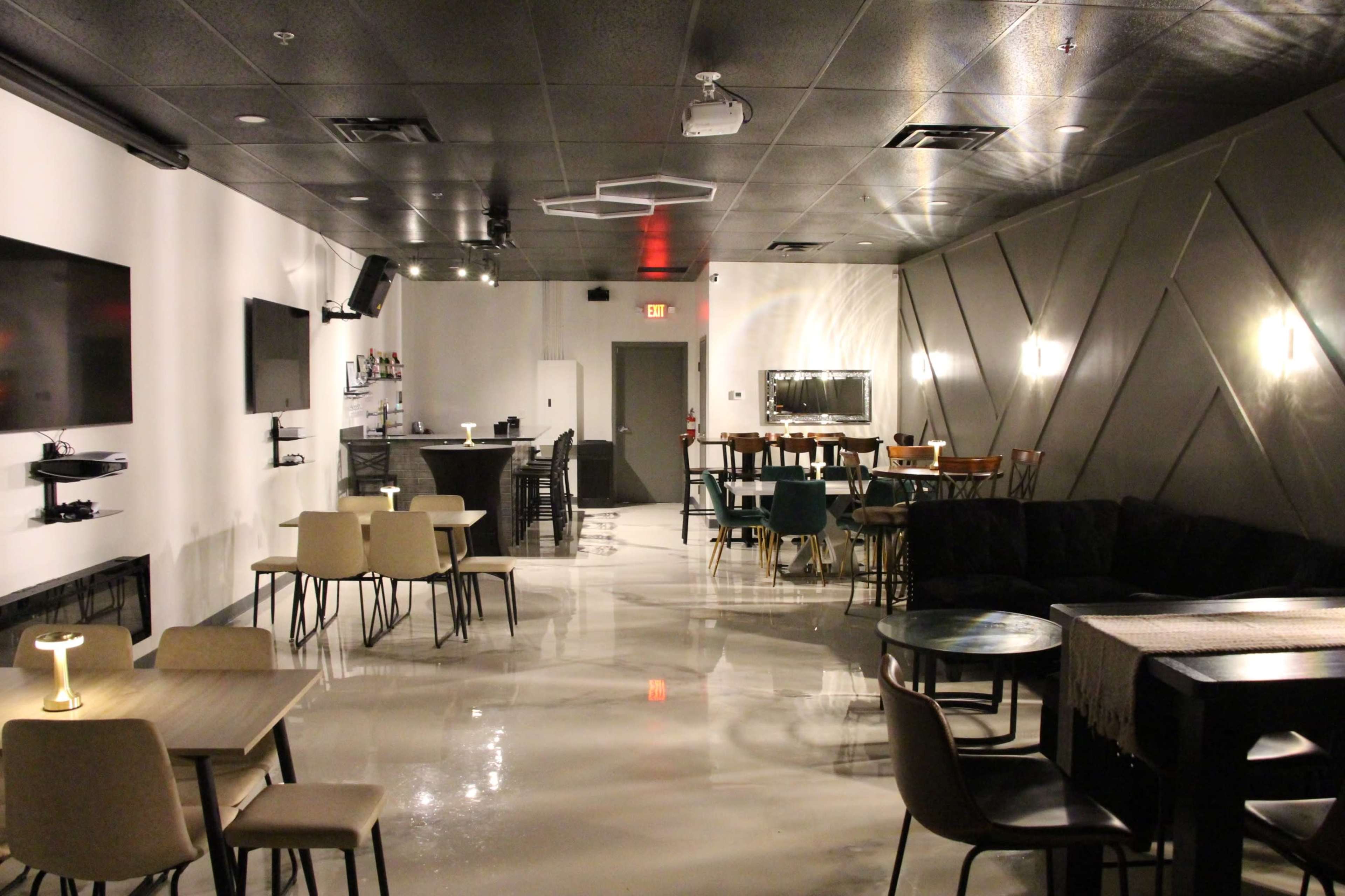 A stylish lounge or bar area with a modern design, featuring various seating arrangements and a bar counter in the background.