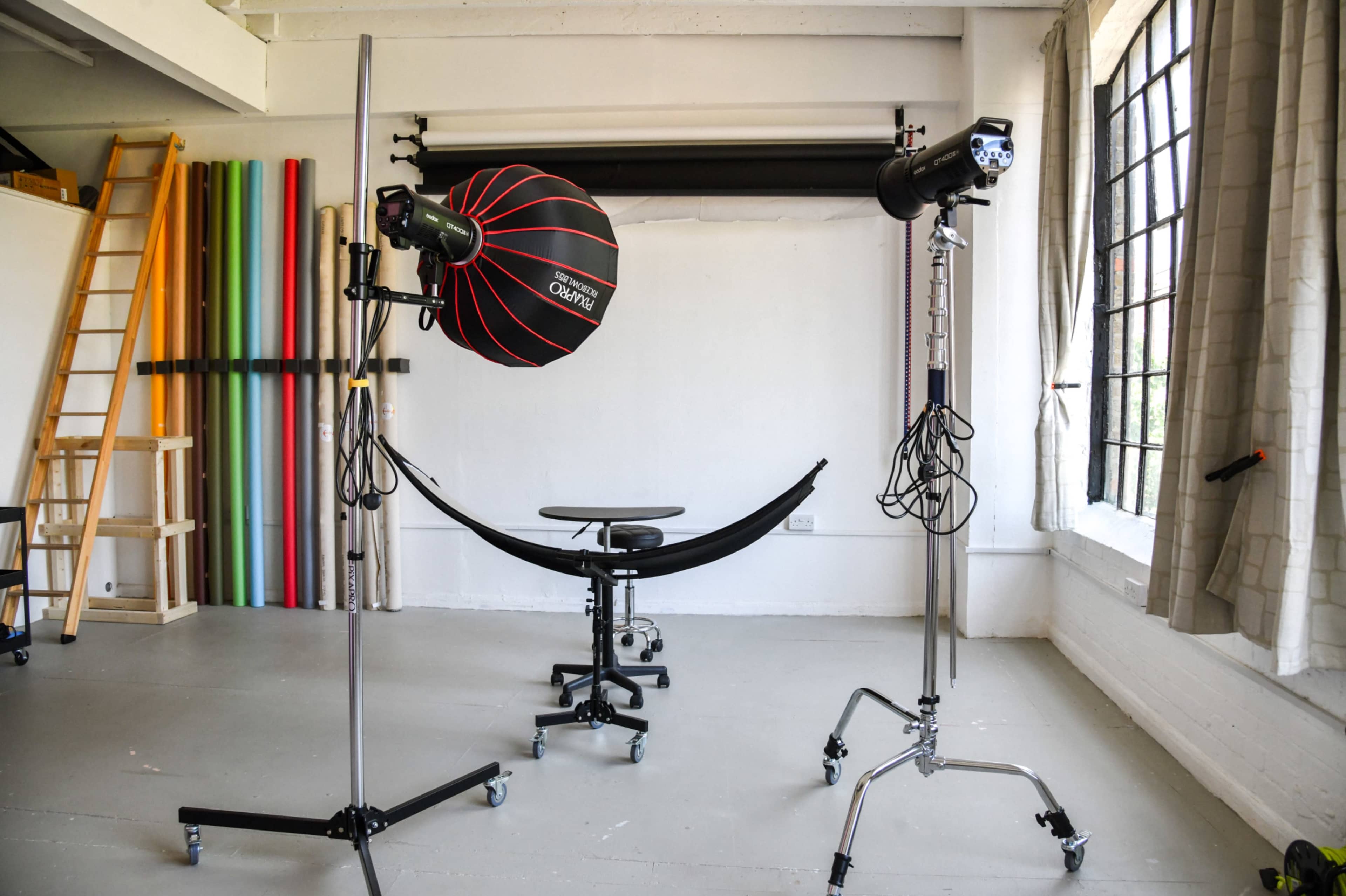 A photography studio with a background of colorful poles, a seated stool, and two lighting setups positioned on stands.