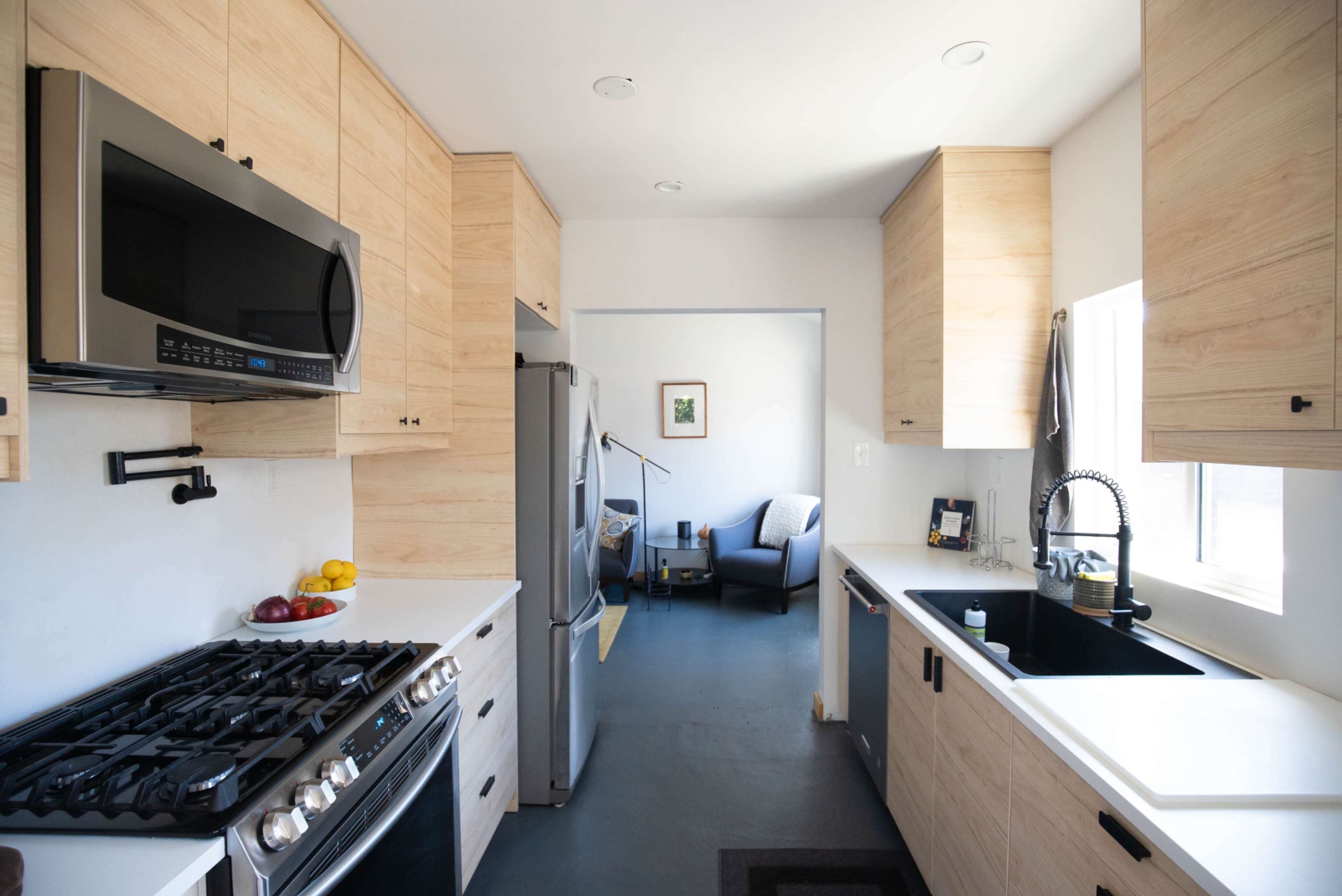 A modern kitchen features wooden cabinetry, stainless steel appliances, and an open layout leading to a living area.