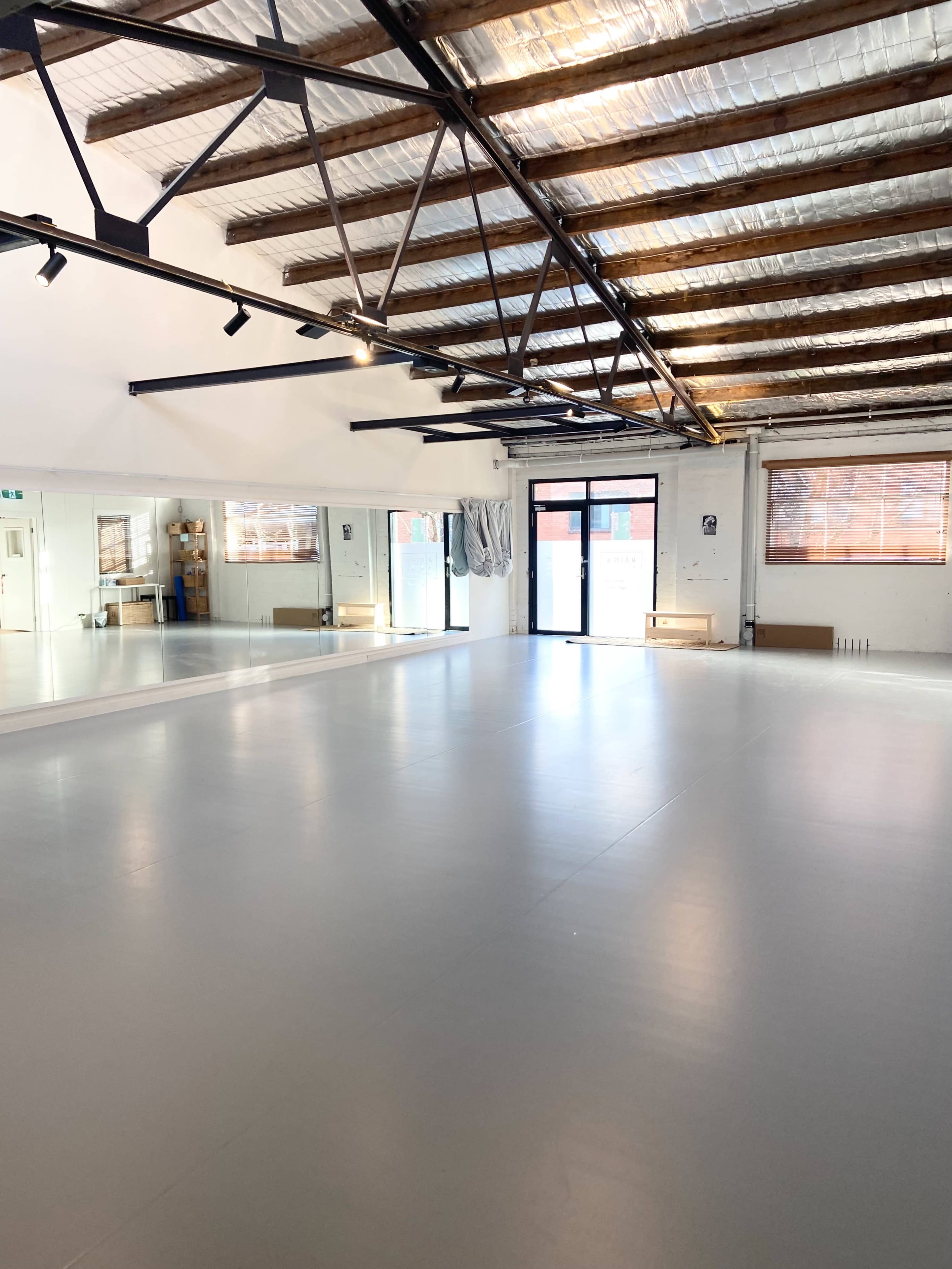 The image shows a spacious dance studio with wooden beams, large mirrors, and a smooth gray floor.